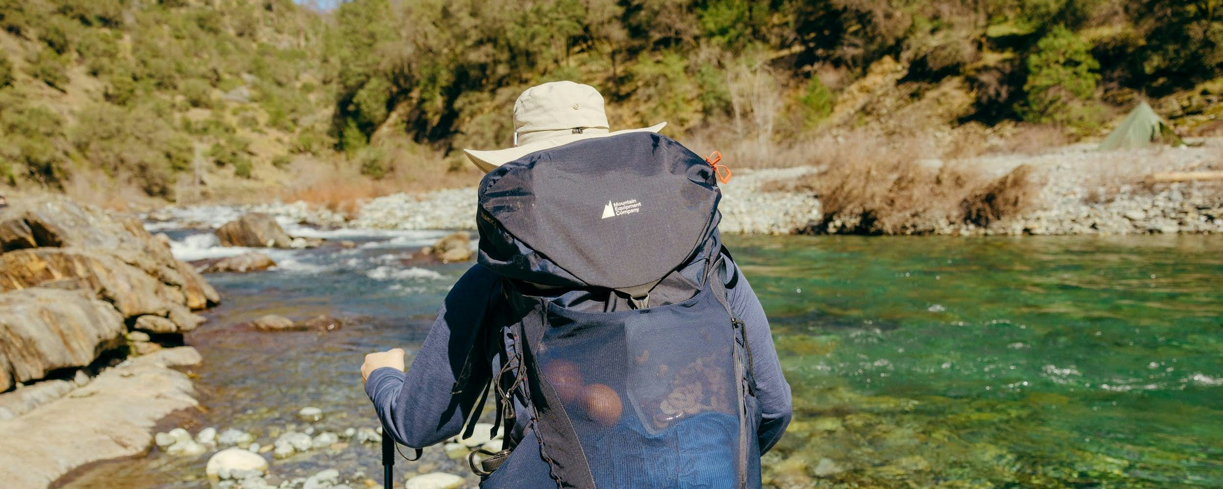 Hiker wearing large backpack with MEC logo with a river in the background