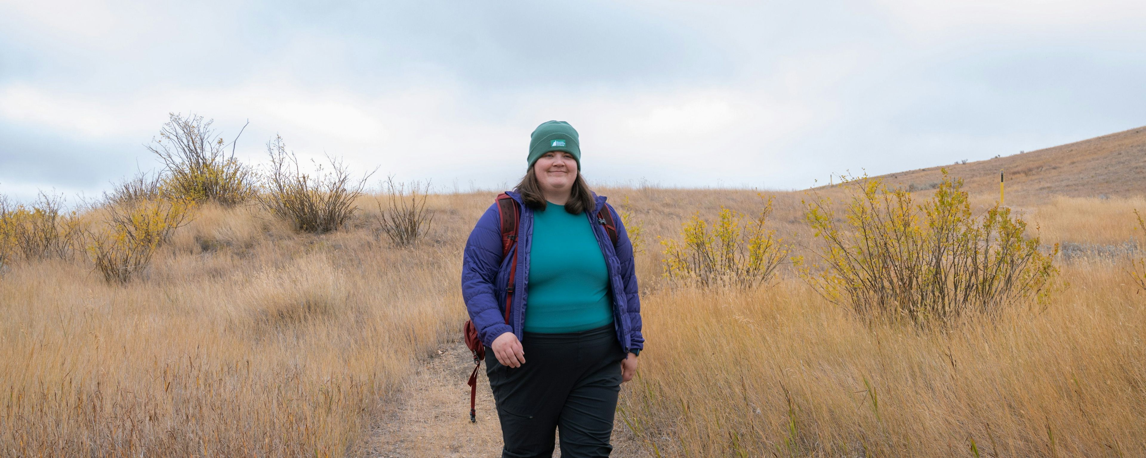Kaila hikes in Grasslands National Park in her MEC Borderland Pants, MEC Uplink Jacket in Wild Berry, T0 Base Layer Long Sleeve Shirt in Alpine Sage and MEC Classic Beanie.