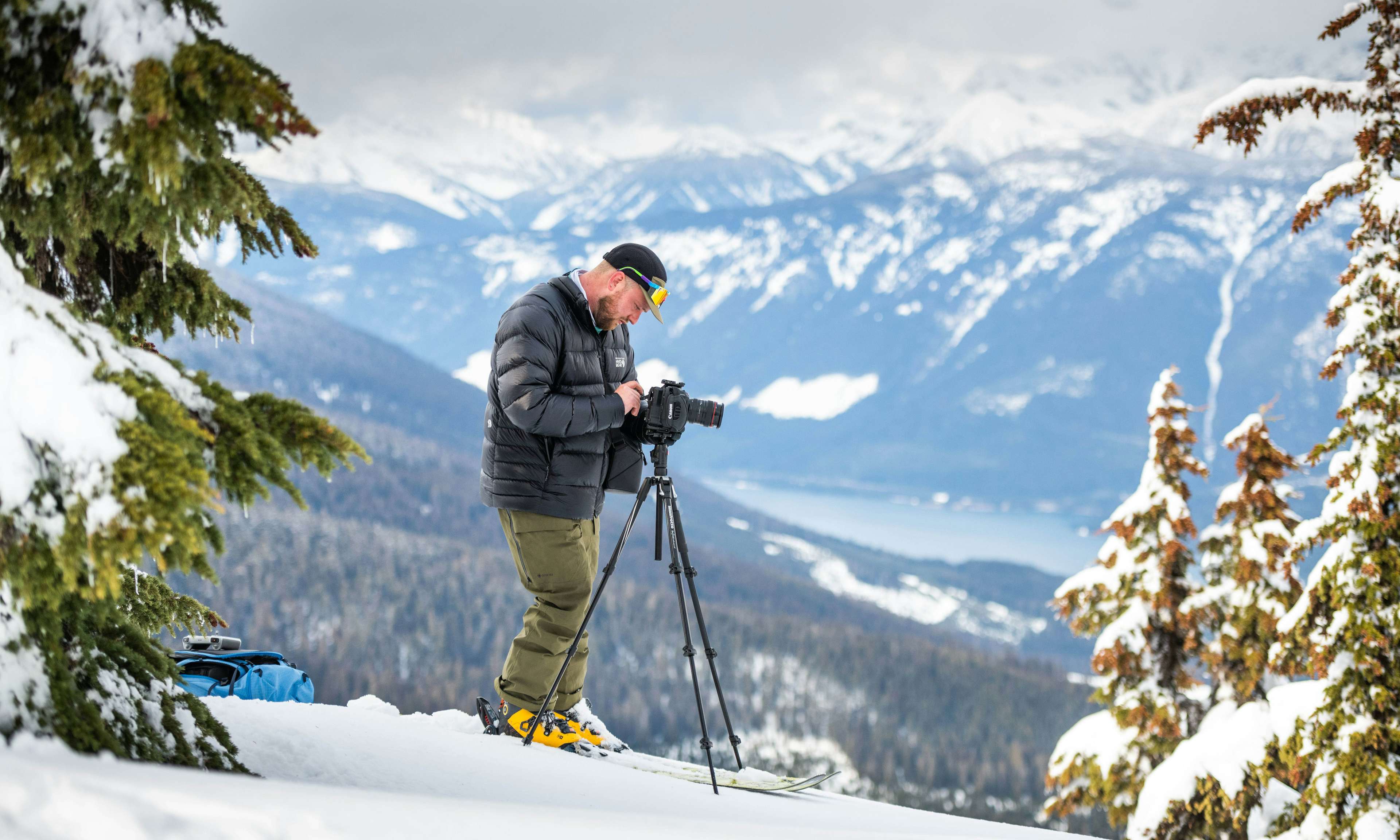 Filmmaker Ryan Collins with a camera in snowy landscape with mountains and lake behind