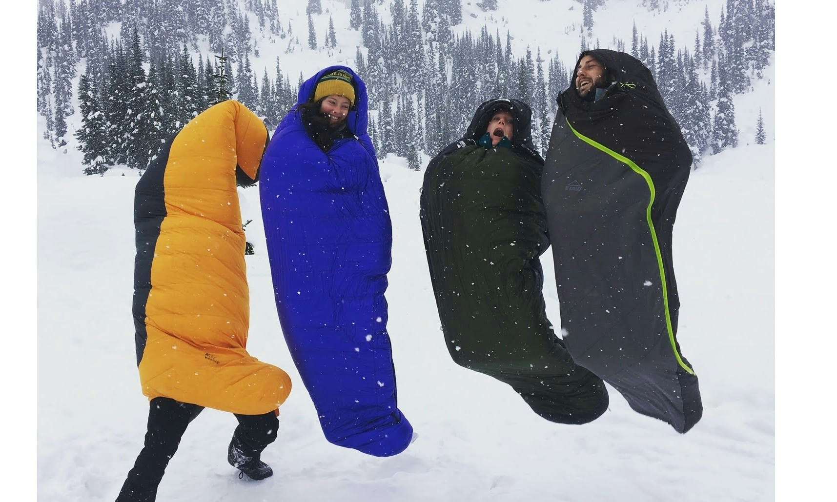 Four people in yellow, blue and black sleeping bags in the snow