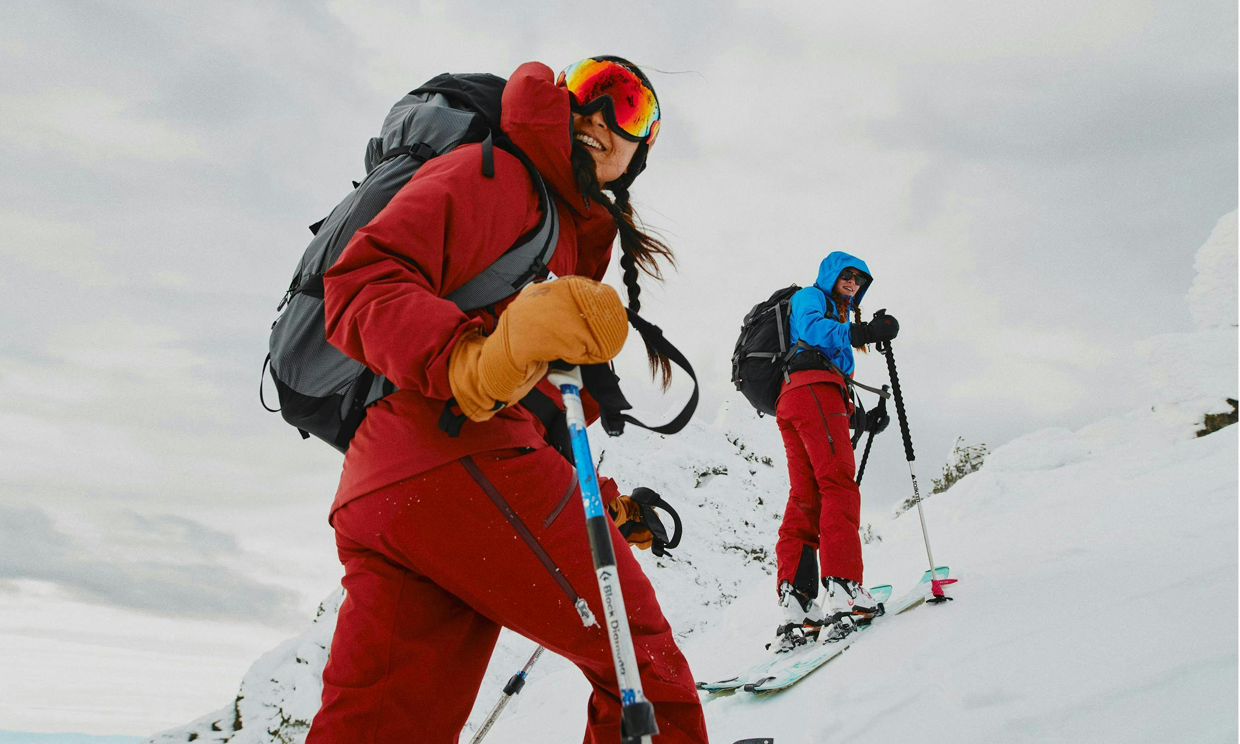 Two skiers skinning uphill, one in monochrome Apex gear, the other in colour-blocked Apex gear