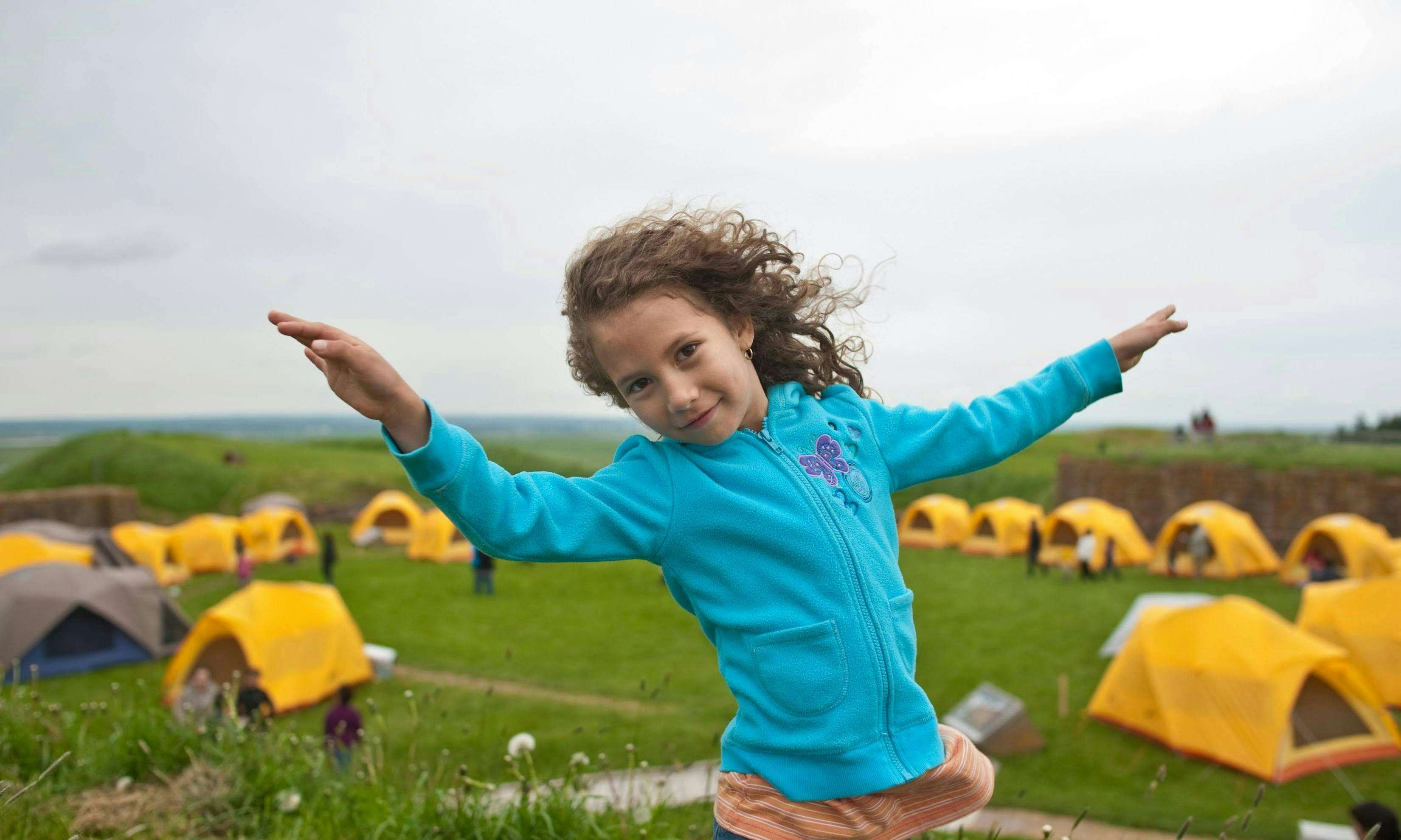 Kid at a learn-to-camp event with yellow tents in a park