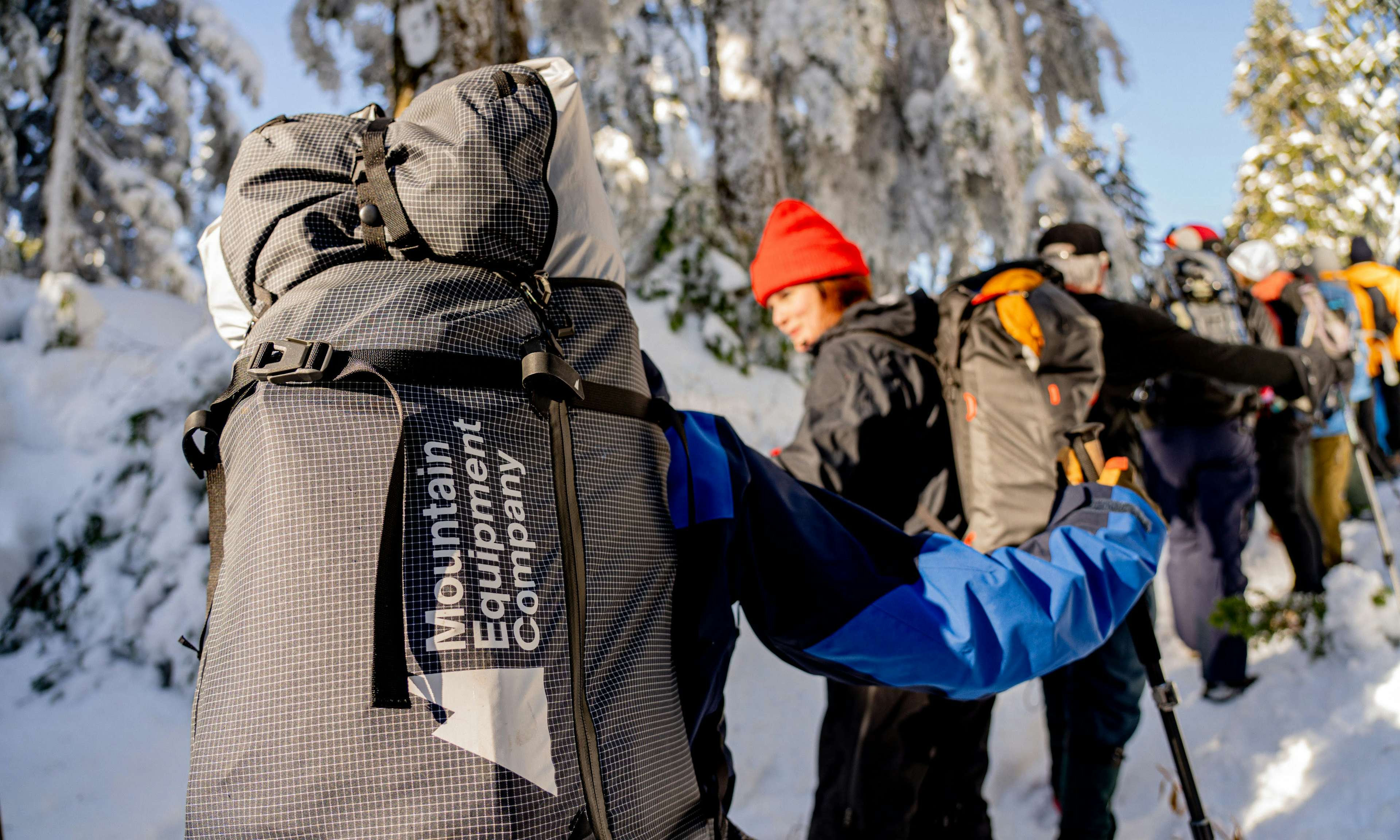 Six people with camping backpacks snowshoeing in the forest