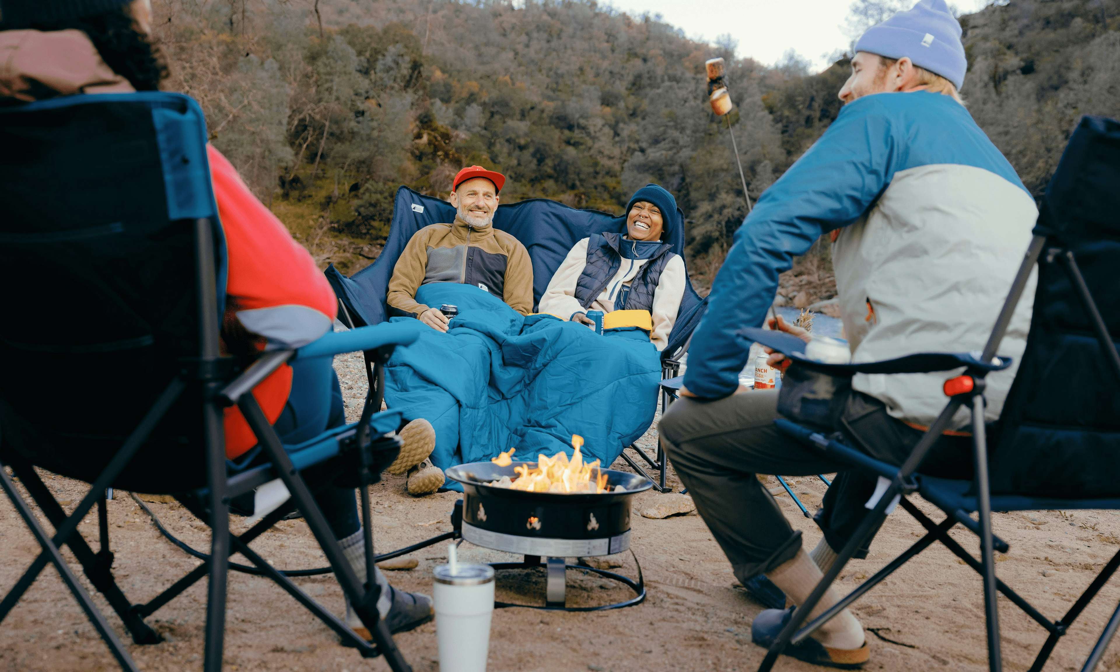 Four campers sitting outside on chairs with a propane fire pit.