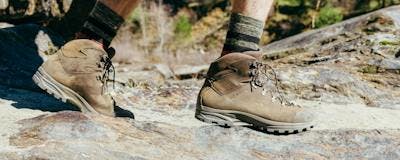 Zoomed in image of a person wearing brown leather hiking boots walking on rocky terrain