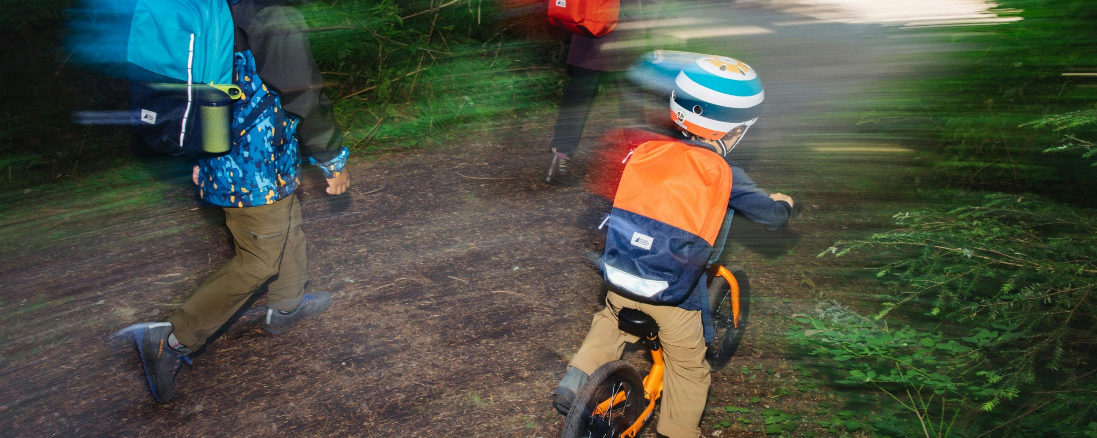 Child riding a push bike with a fun helmet on, and family members walking alongside
