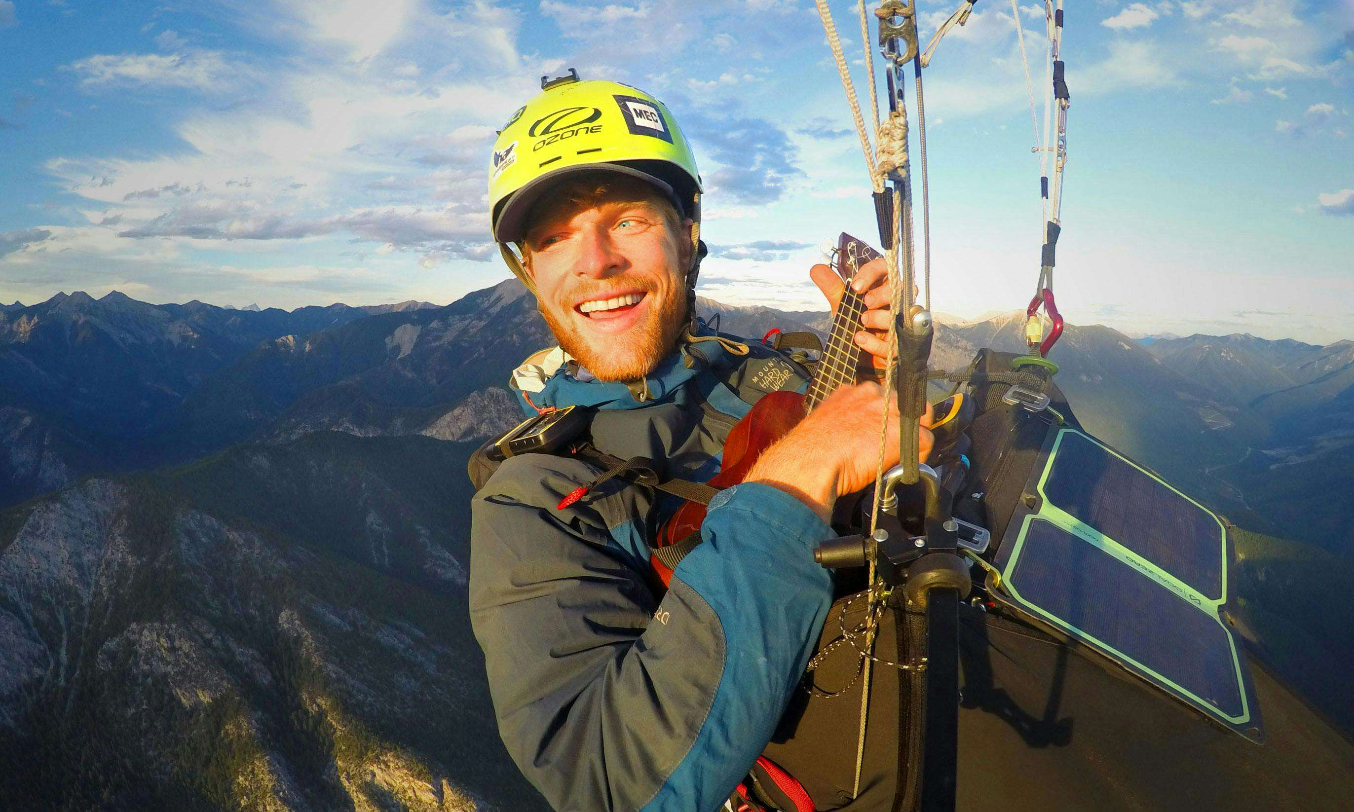 Benjamin Jordan playing ukulele while paragliding above the mountains