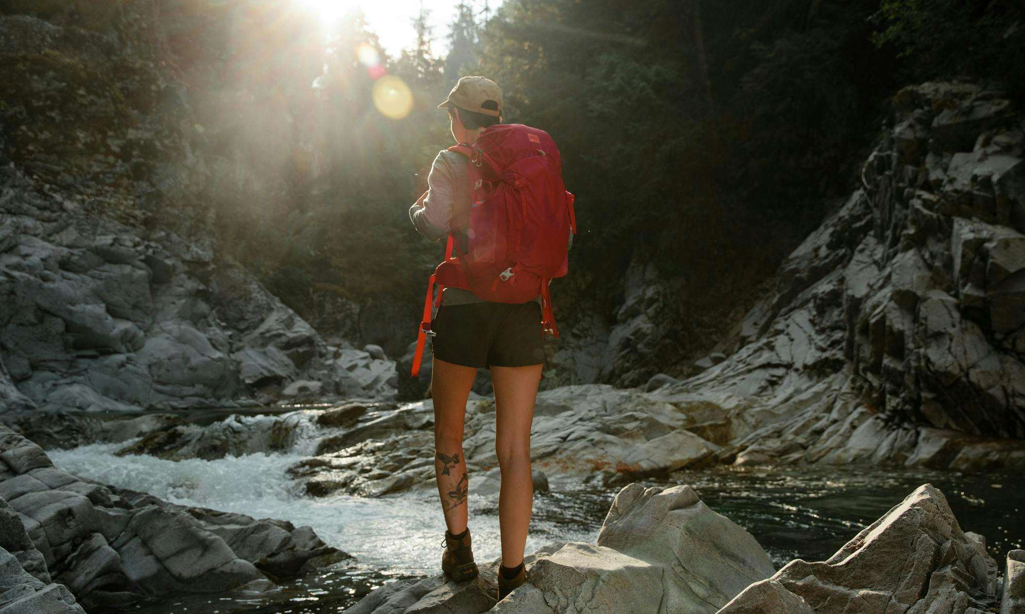 Person walking with a pink backpack near a creek with rocks
