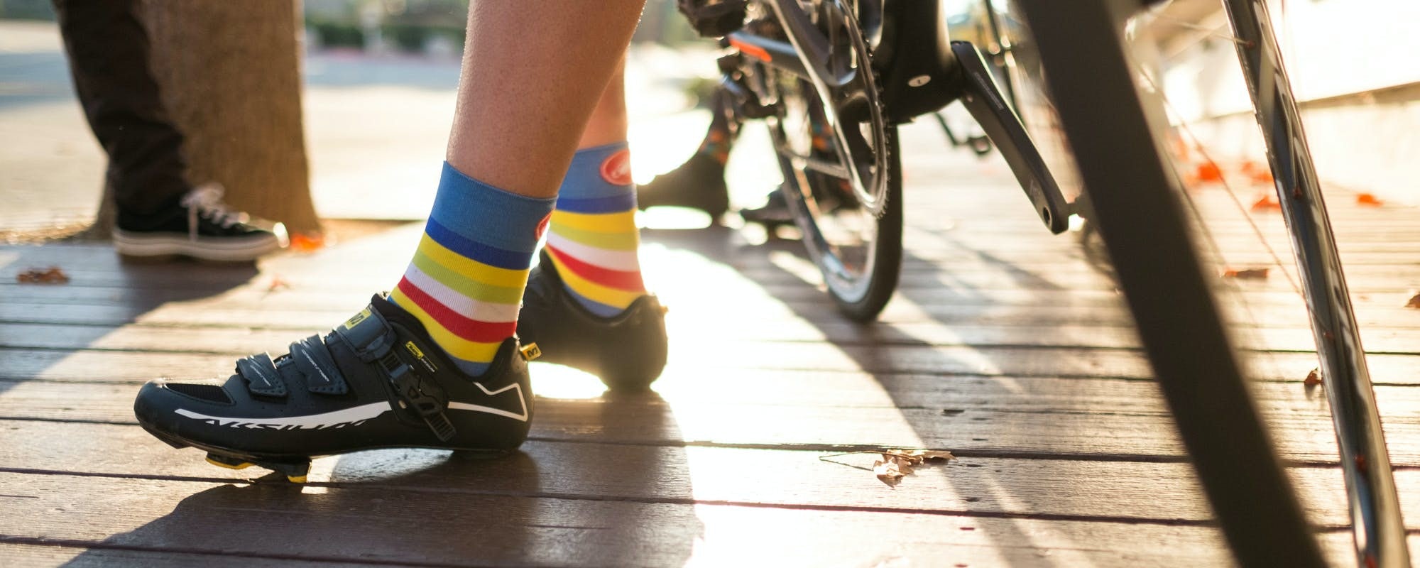 Vue des chaussettes et des chaussures d'un cycliste qui s'appuie sur son vélo.