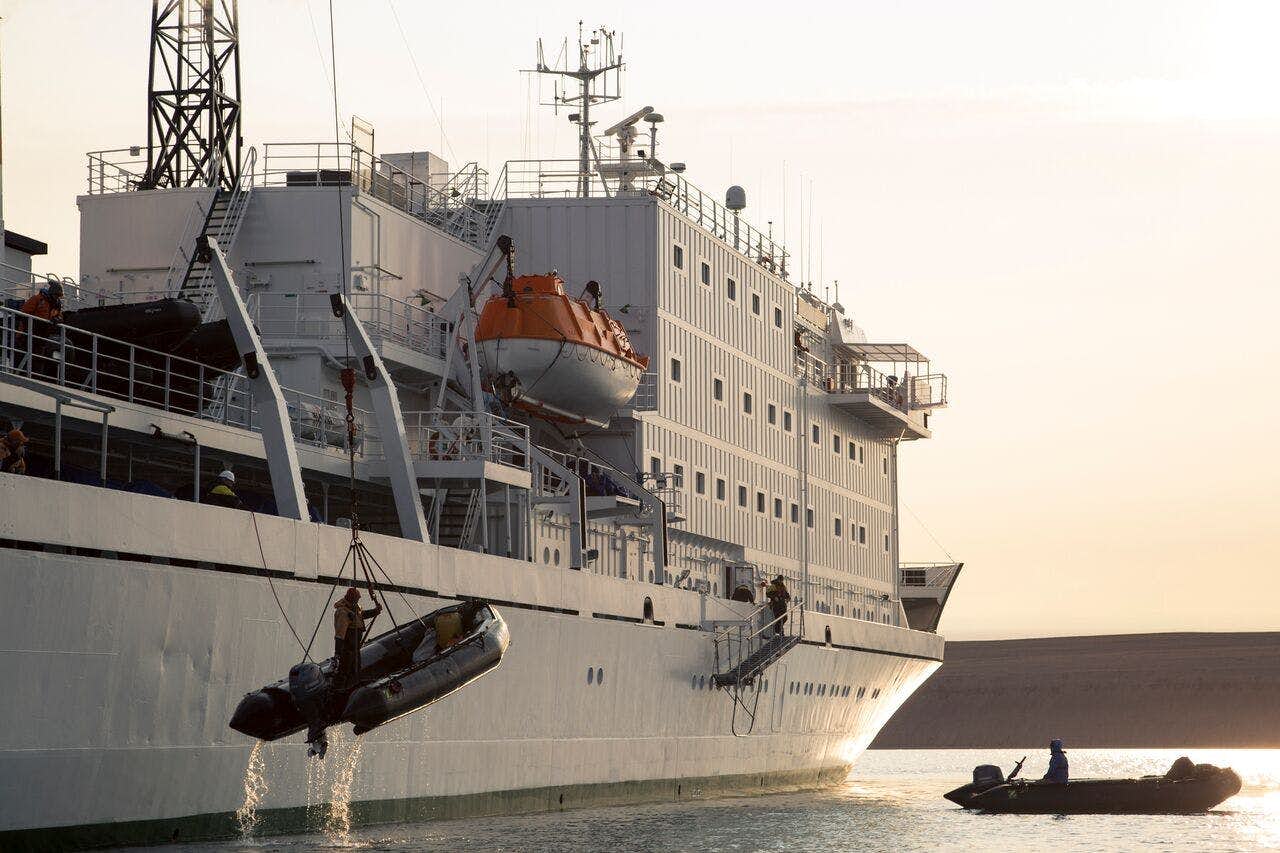 A ship lowers a zodiac inflatable boat as another zodiac floats nearby.
