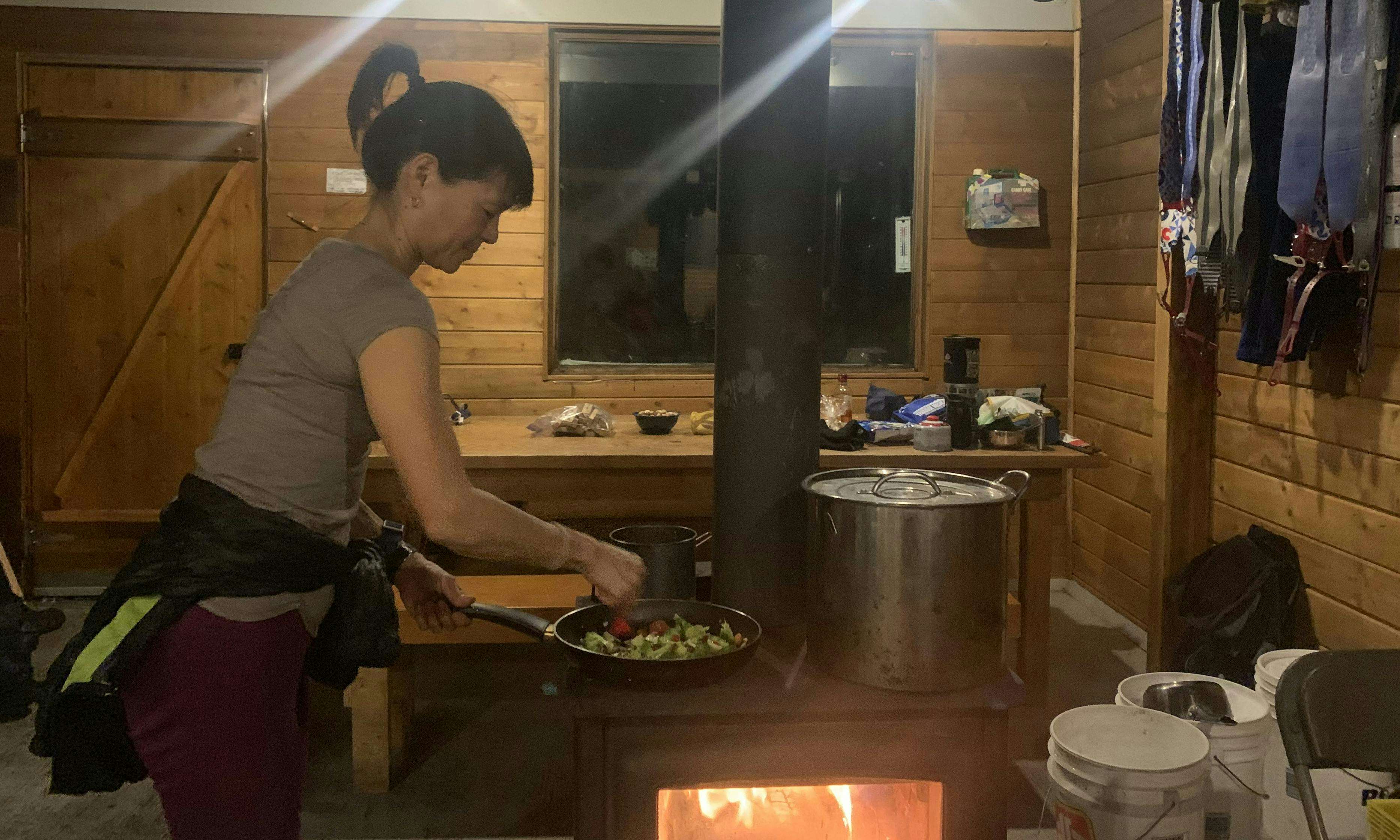 Person making dinner on a wood stove in a backcountry hut