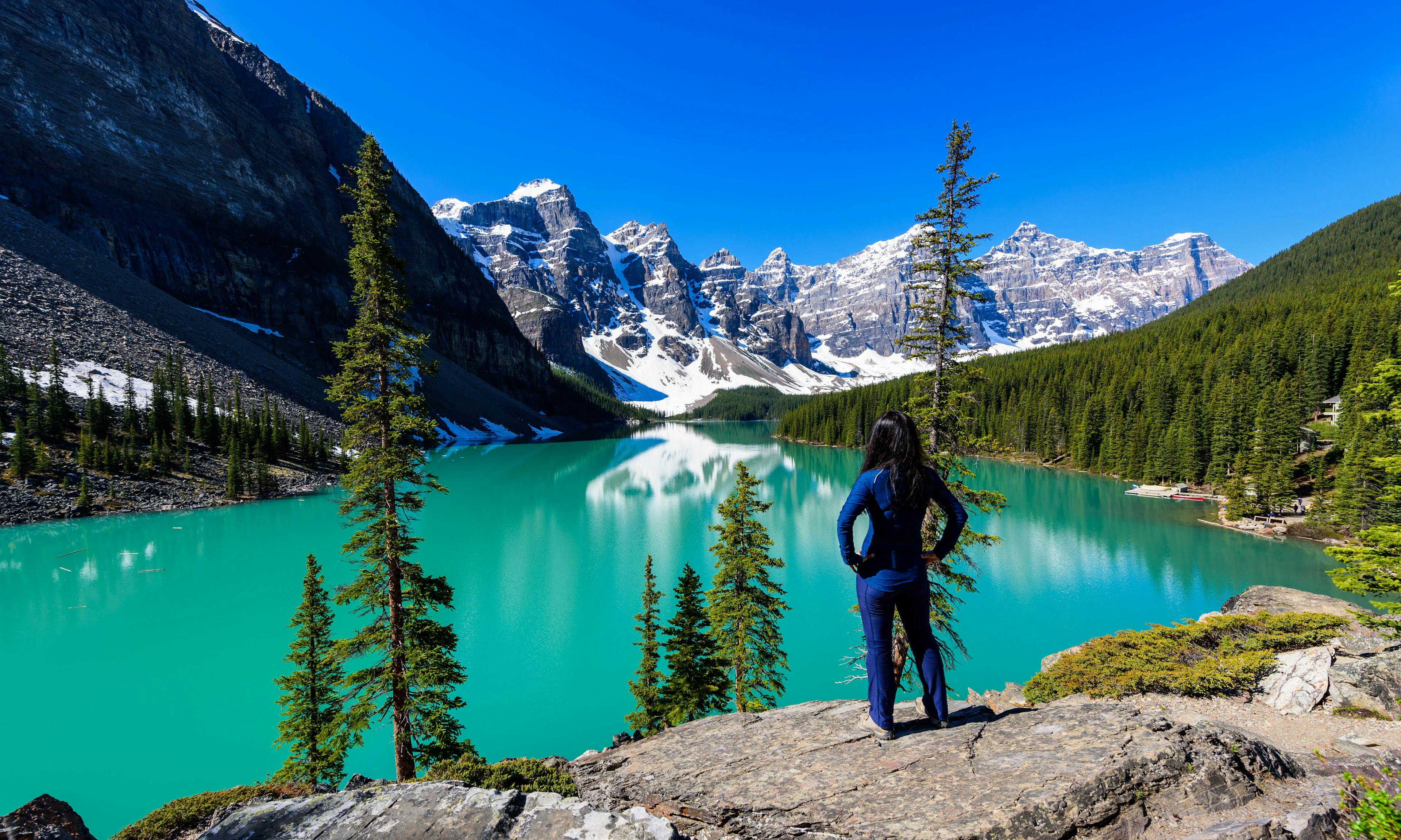 Woman on cliff admiring Moraine Lake and mountains scenic view, Rocky Mountains, Banff National Park, Alberta, Canada