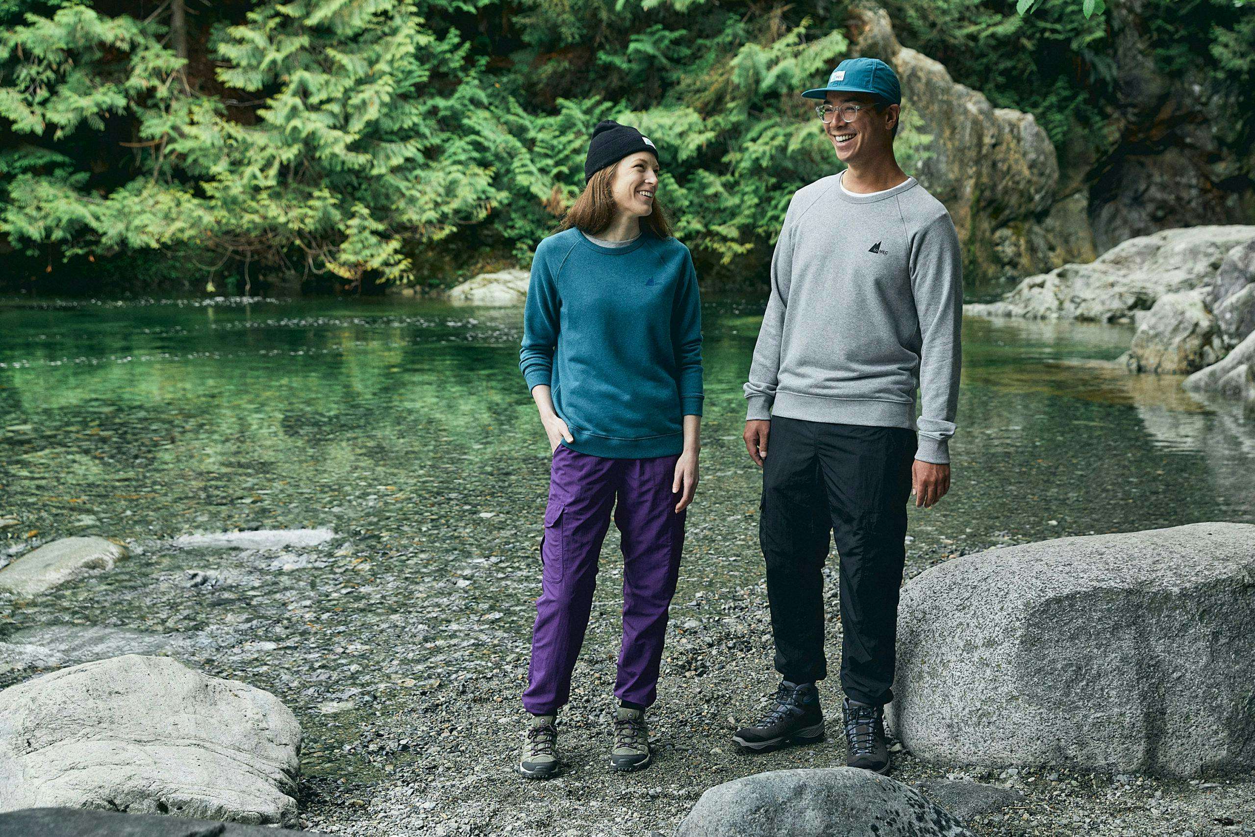 Two people wearing cuffed MEC Rad Pants in purple and black, standing next to a river