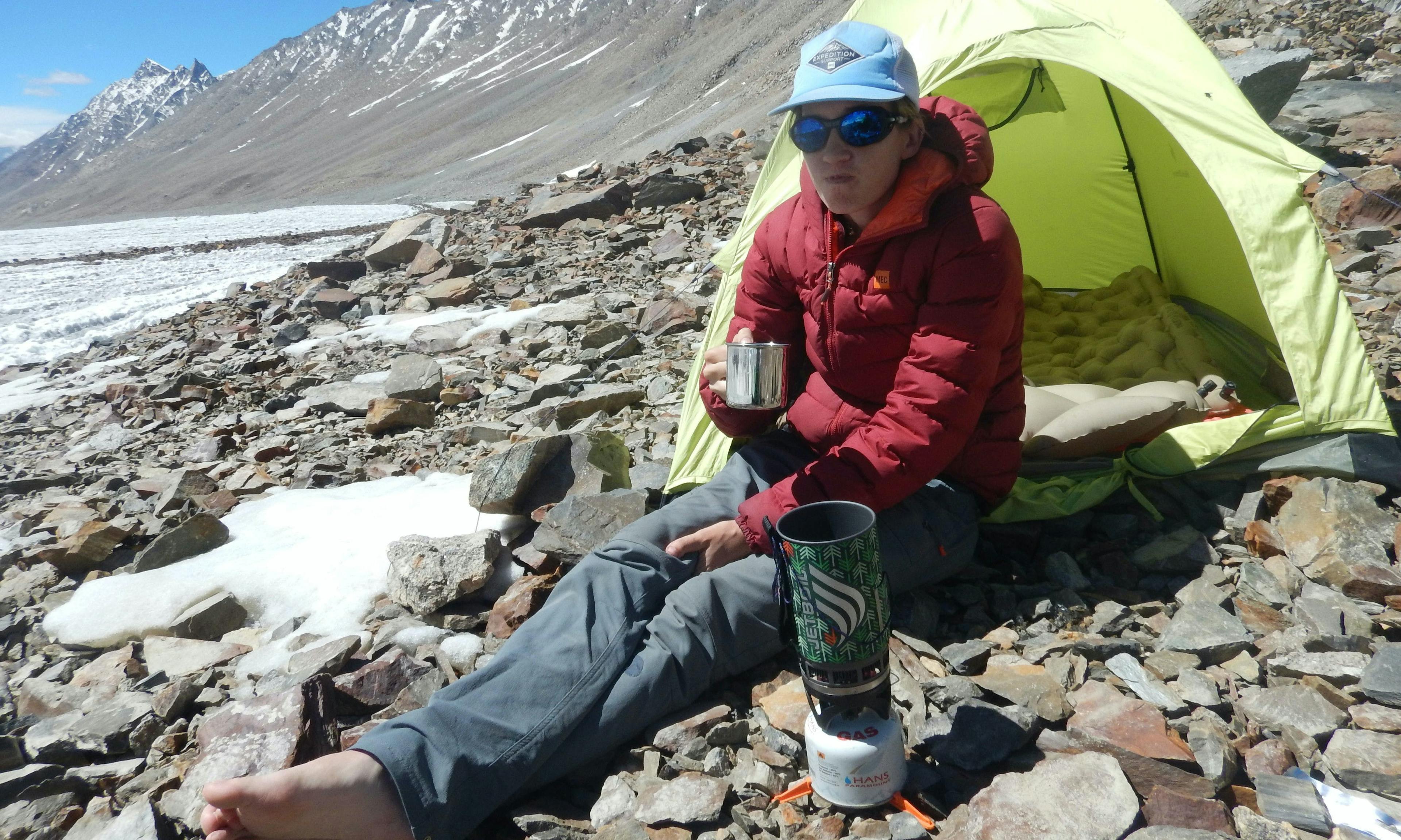 Climber sitting next to a small tent and sipping a hot drink from a coffee mug