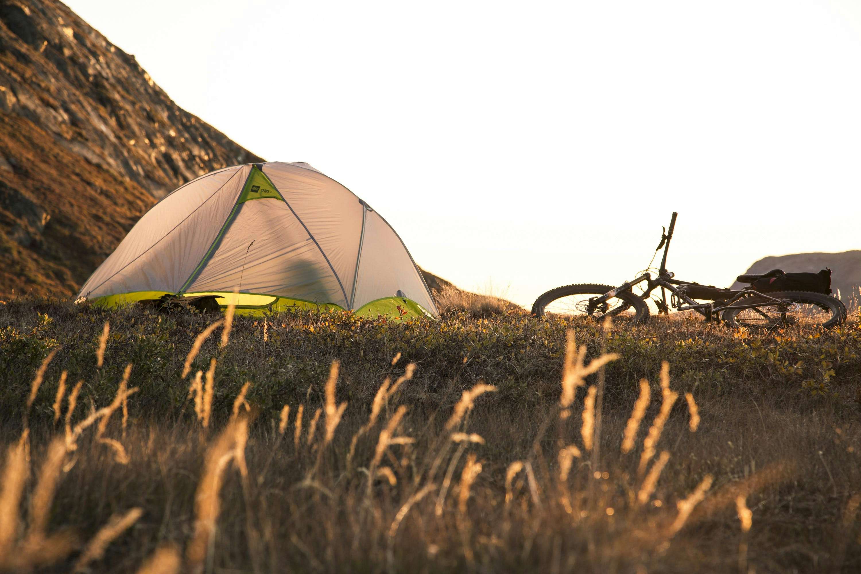 A bike lies on its side next to a small tent, silhouetted against a bright sky.