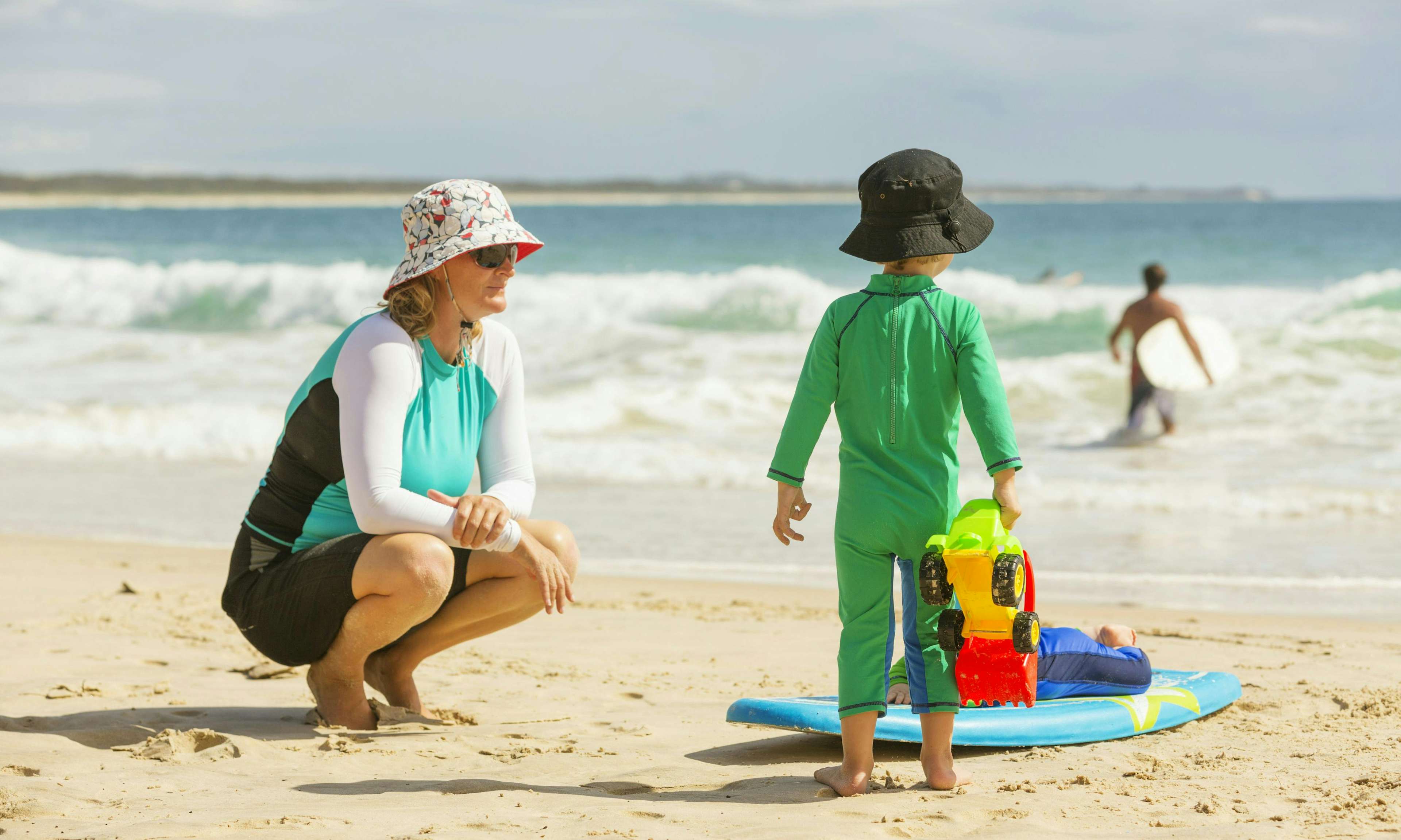 Mom and child on the beach wearing sun protective clothing