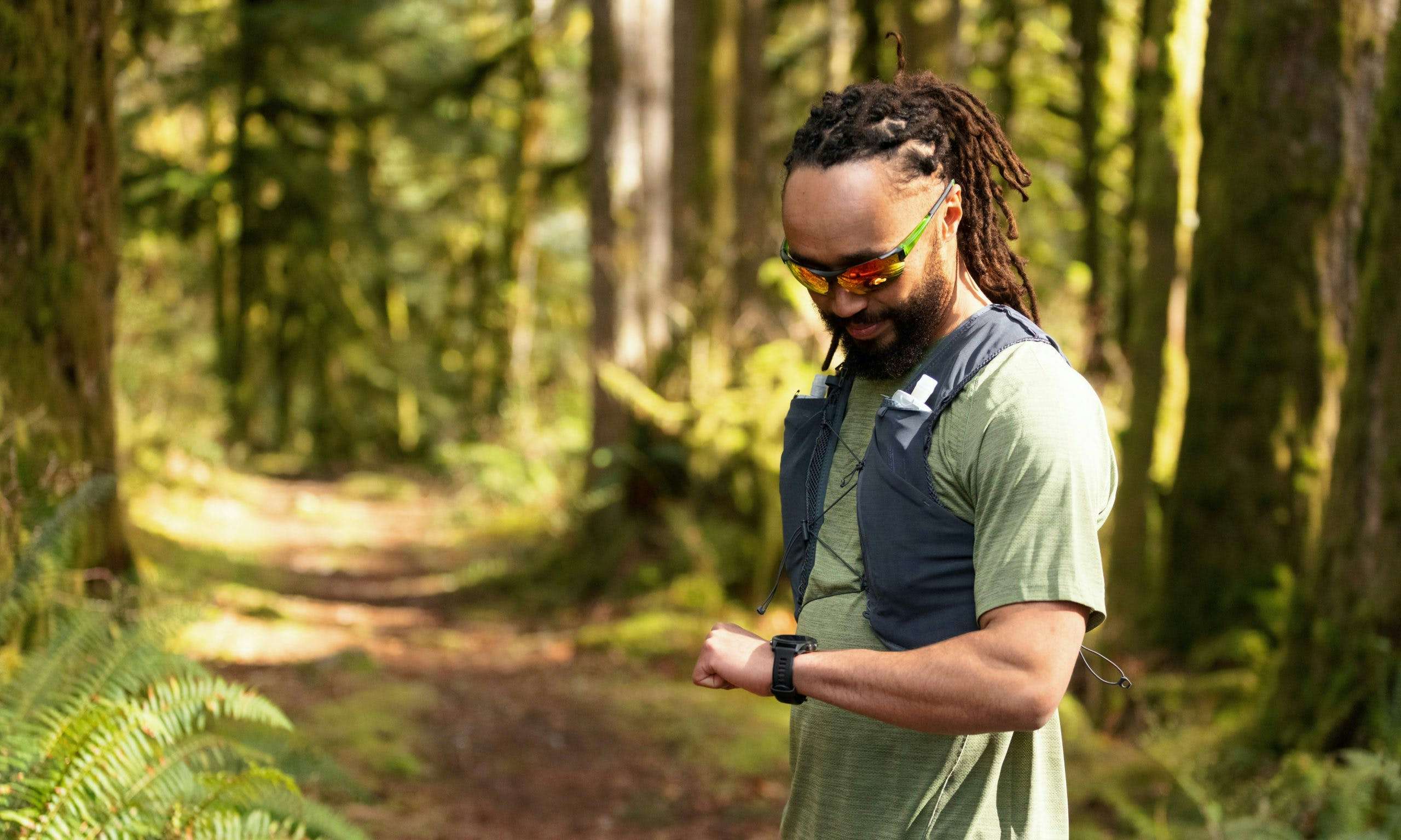 Trail runner wearing a pack and looking at their watch in the forest