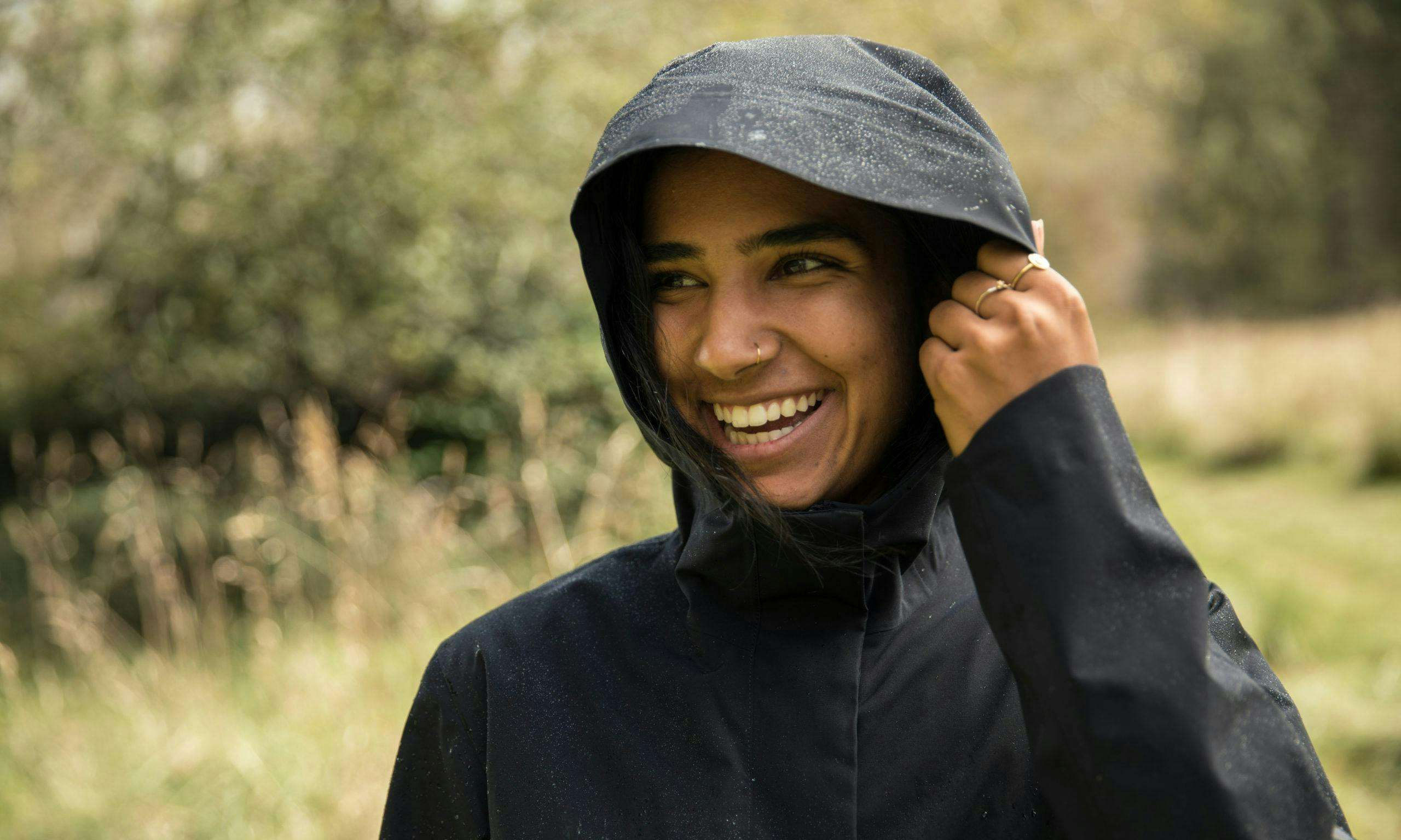 Smiling person wearing a rain jacket with water beading on the hood