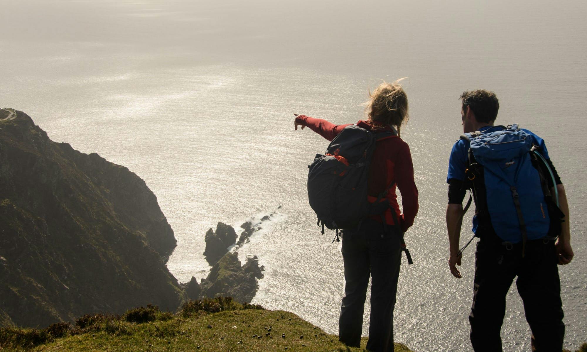 Two hikers on windy high coastline in Ireland, one is pointing