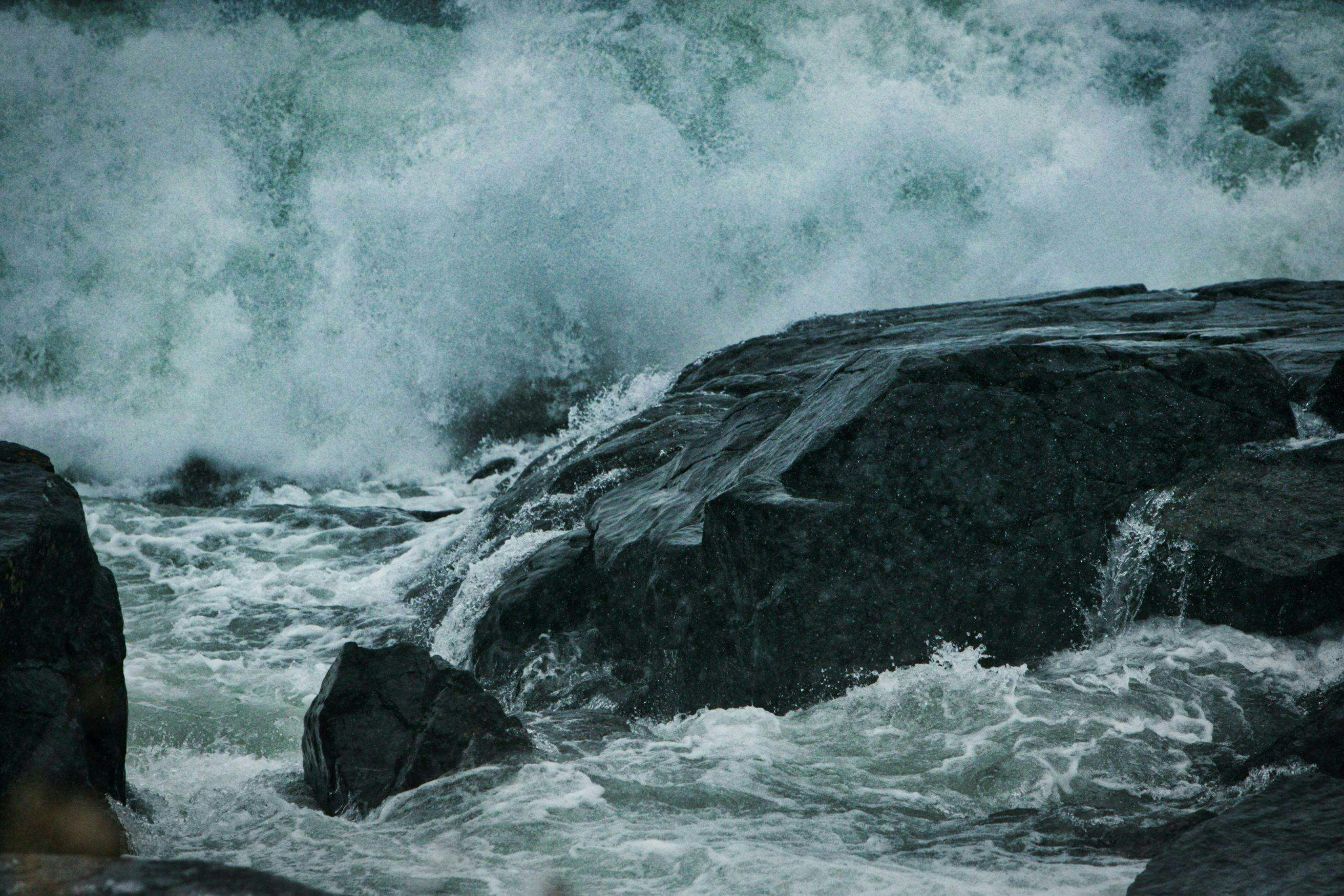 Large wave crashing onto dark grey rocks