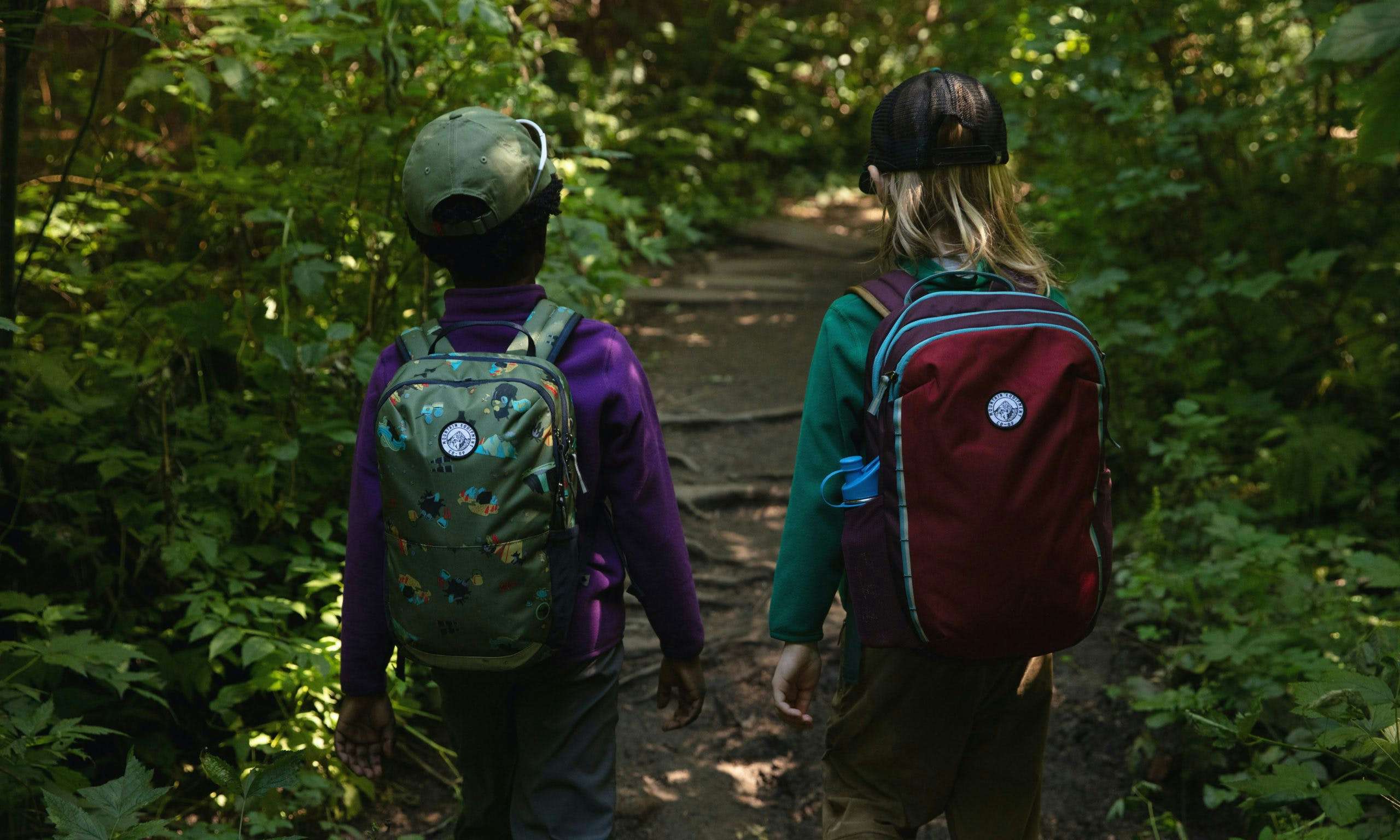 Two kids walking on a forest trail and wearing backpacks