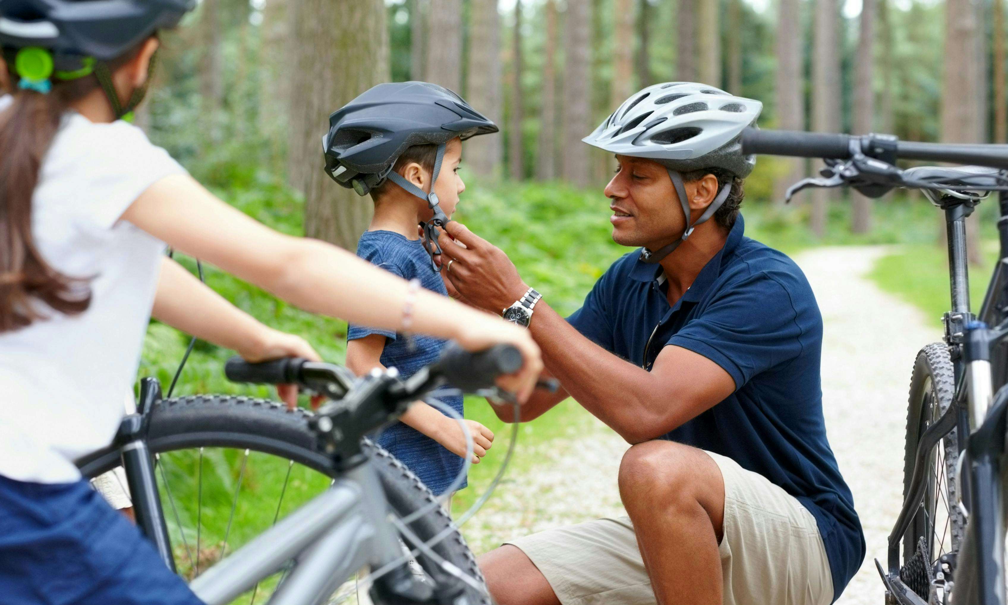 Dad putting a helmet on a young boy about to ride a bike