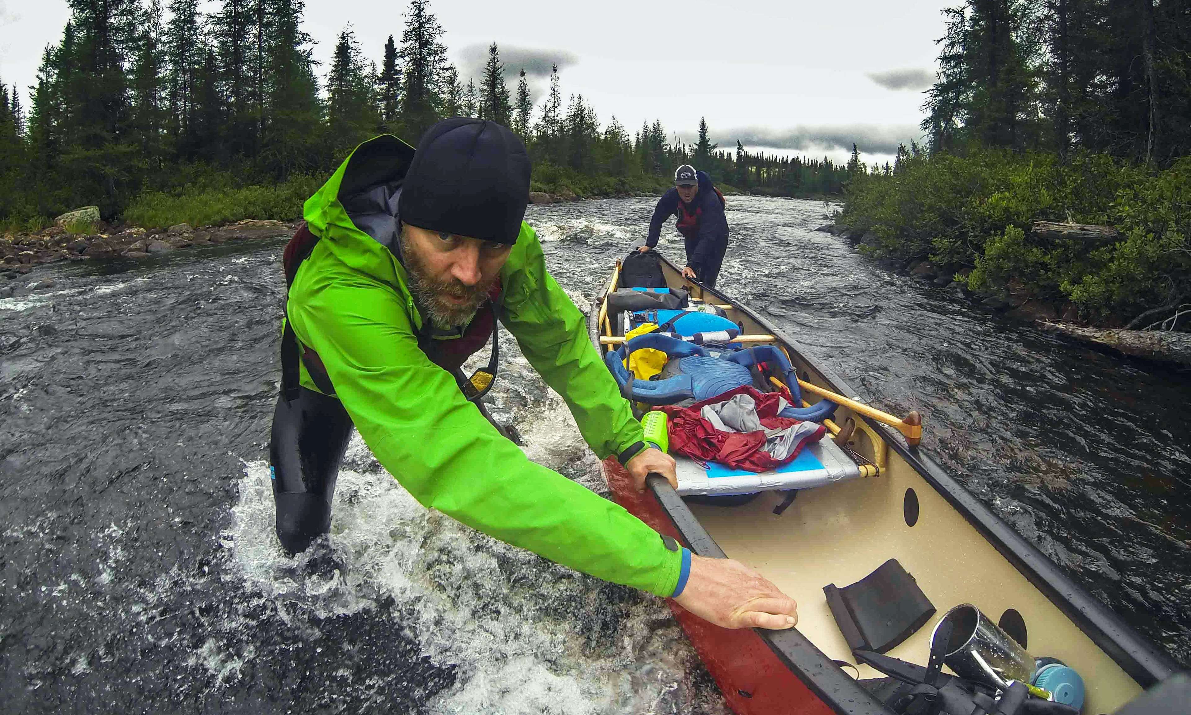 Two men push a canoe through a rushing river.