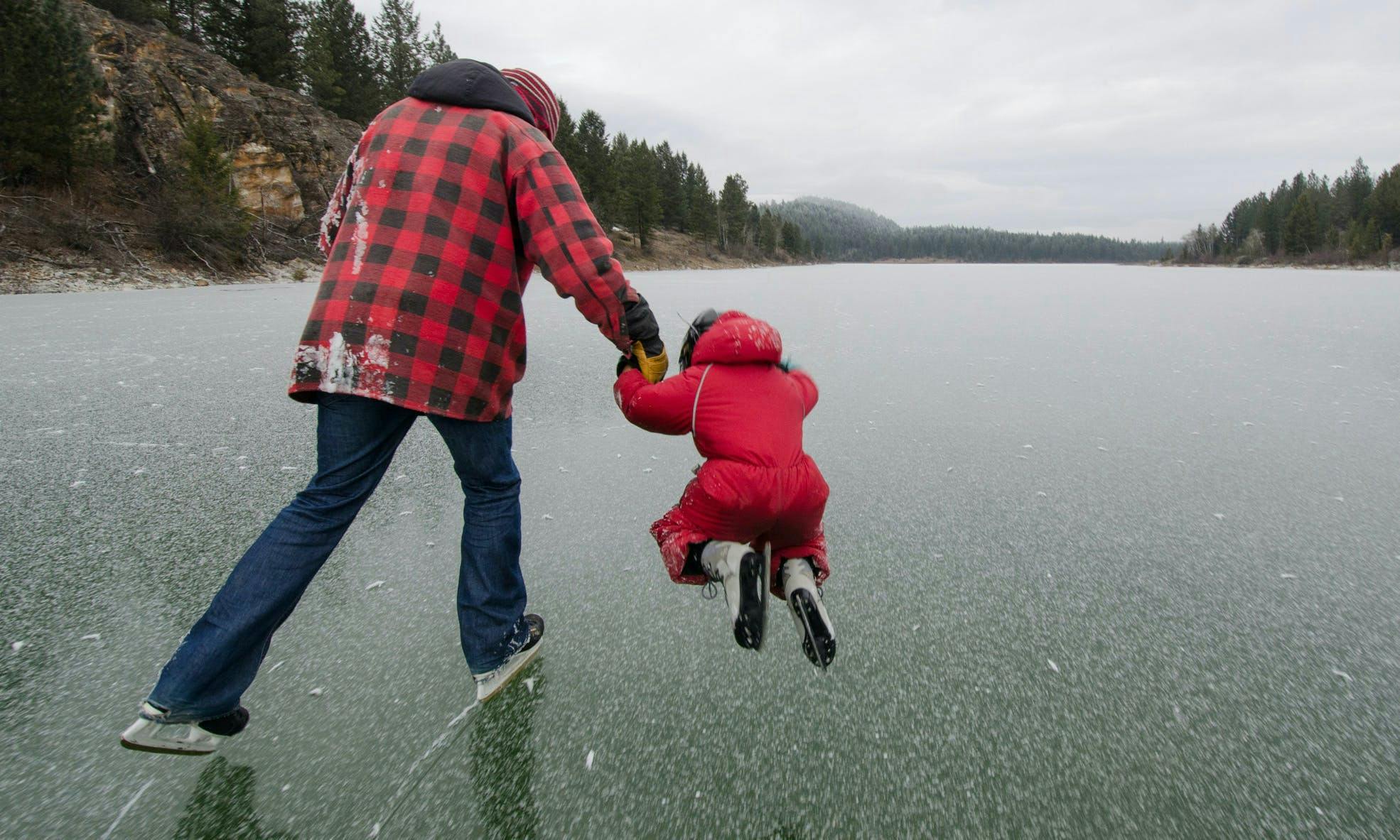 Dad and child skating outdoors on a frozen lake