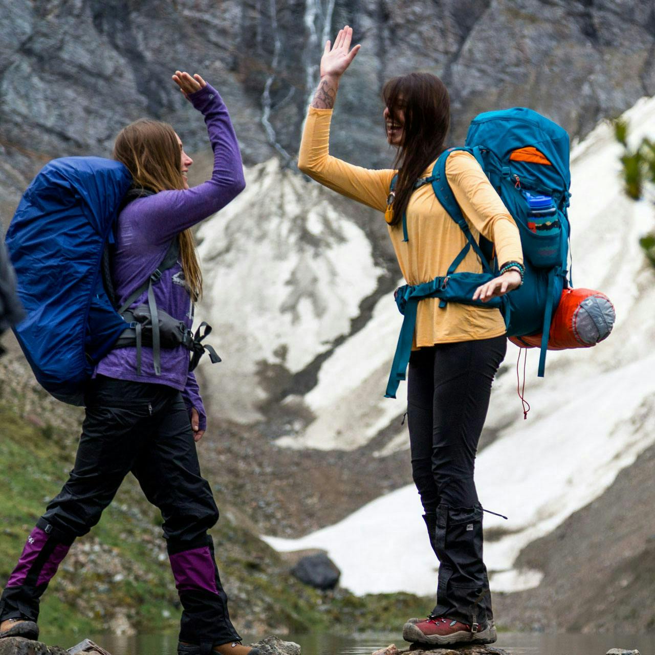 Two backpackers high-fiving with a mountain view in the background