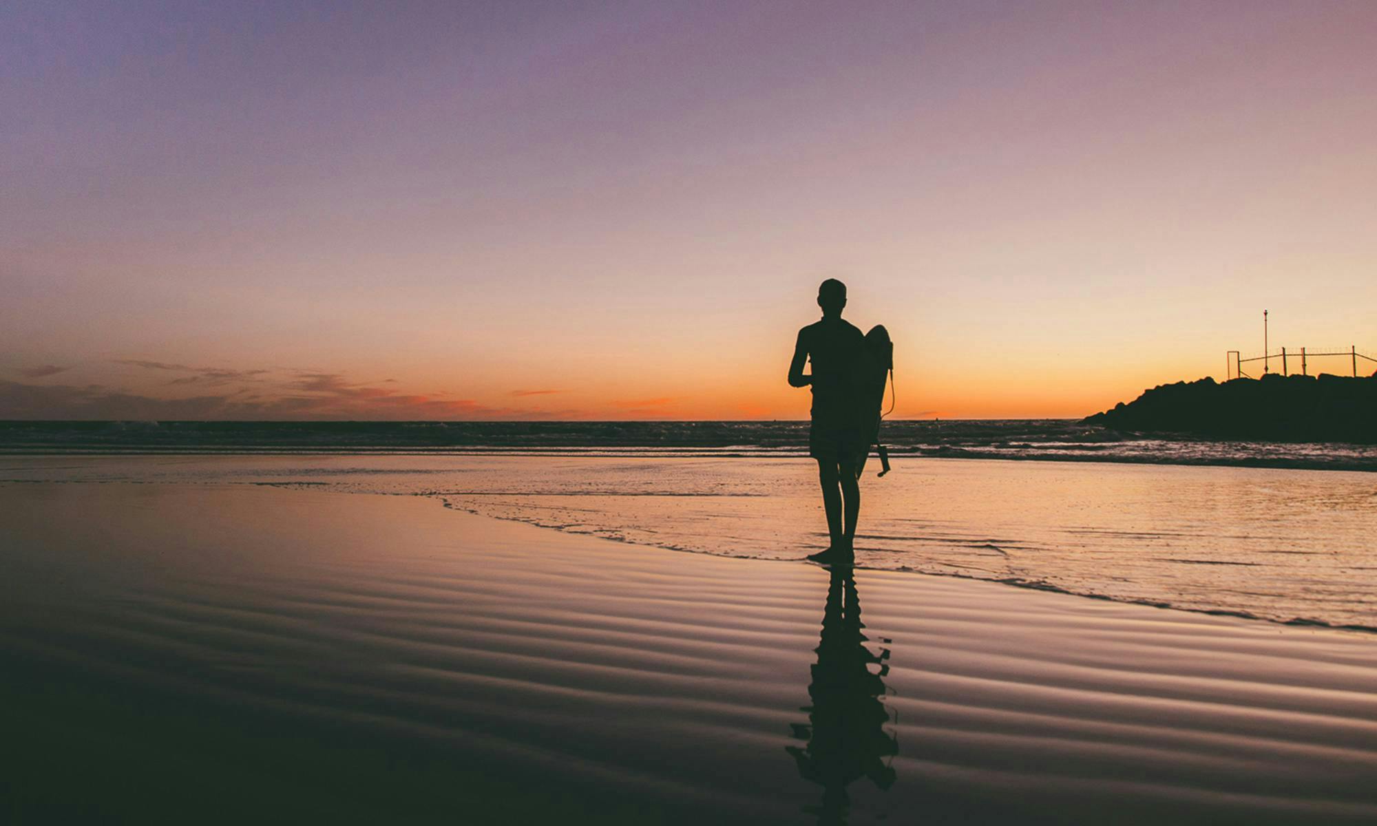 Surfer standing on the beach at sunset