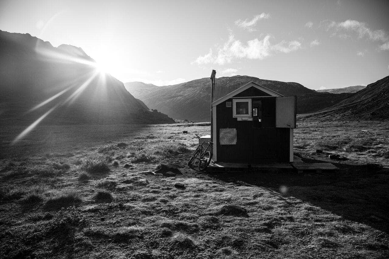 A bike stands next to a small hut, as the sun breaks over a mountain in the background