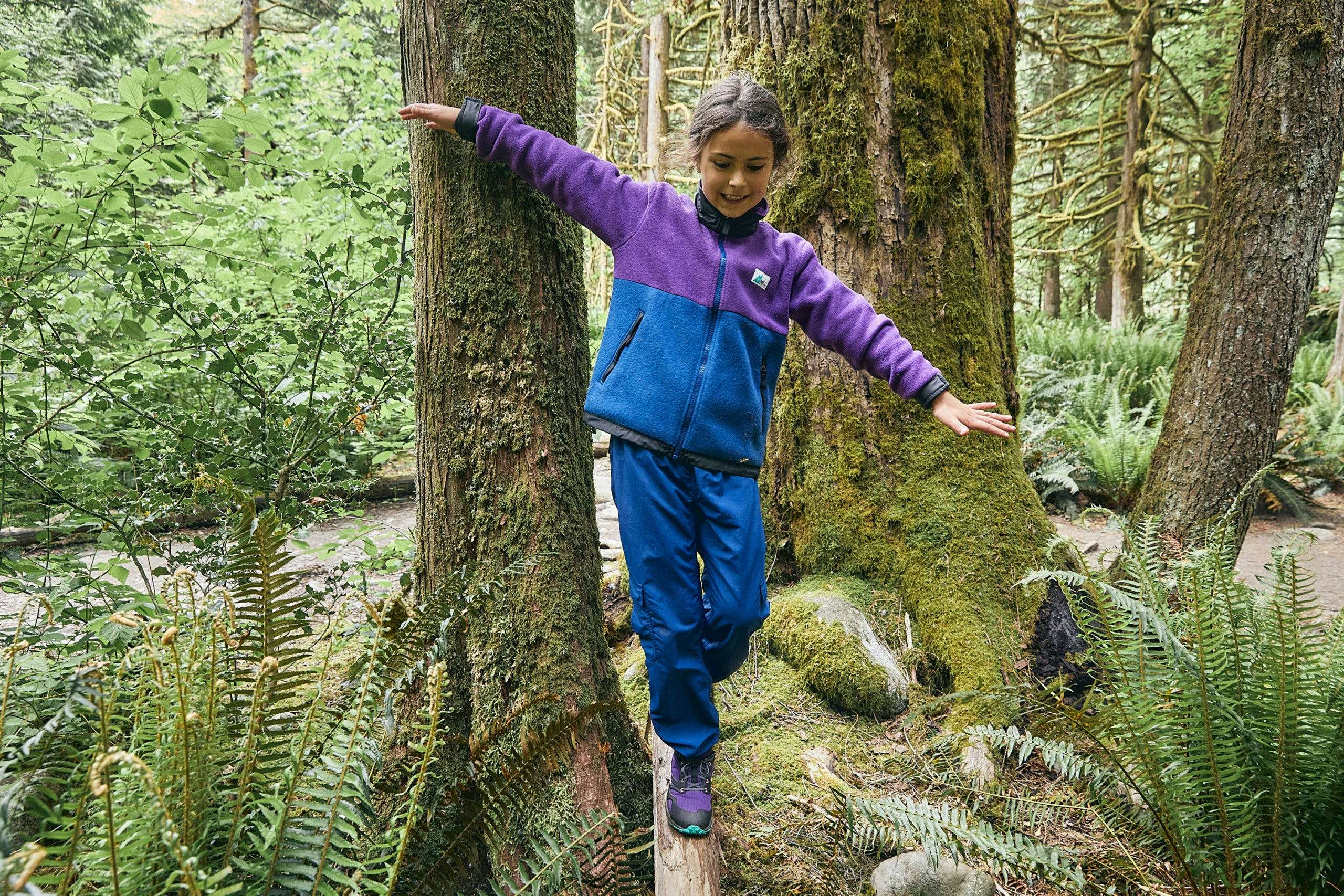 Child wearing a vintage-looking MEC fleece jacket walking across a log while smiling
