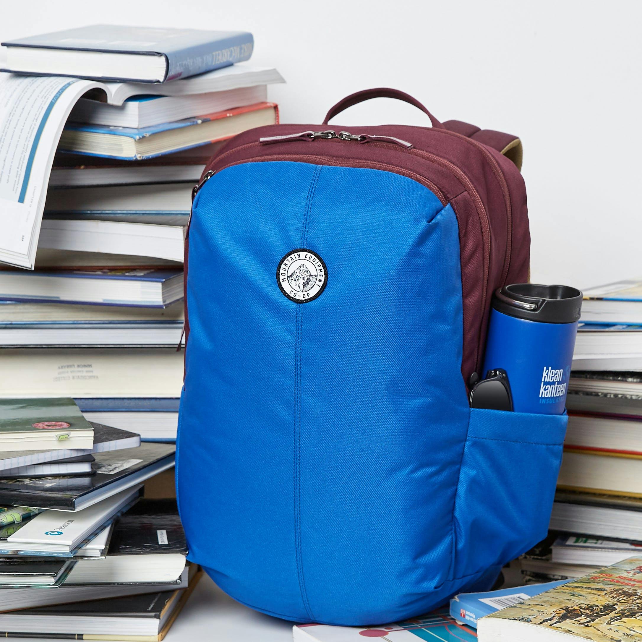 Blue MEC backpack with a blue Kleen Kanteen waterbottle, surrounded by stacks of textbooks
