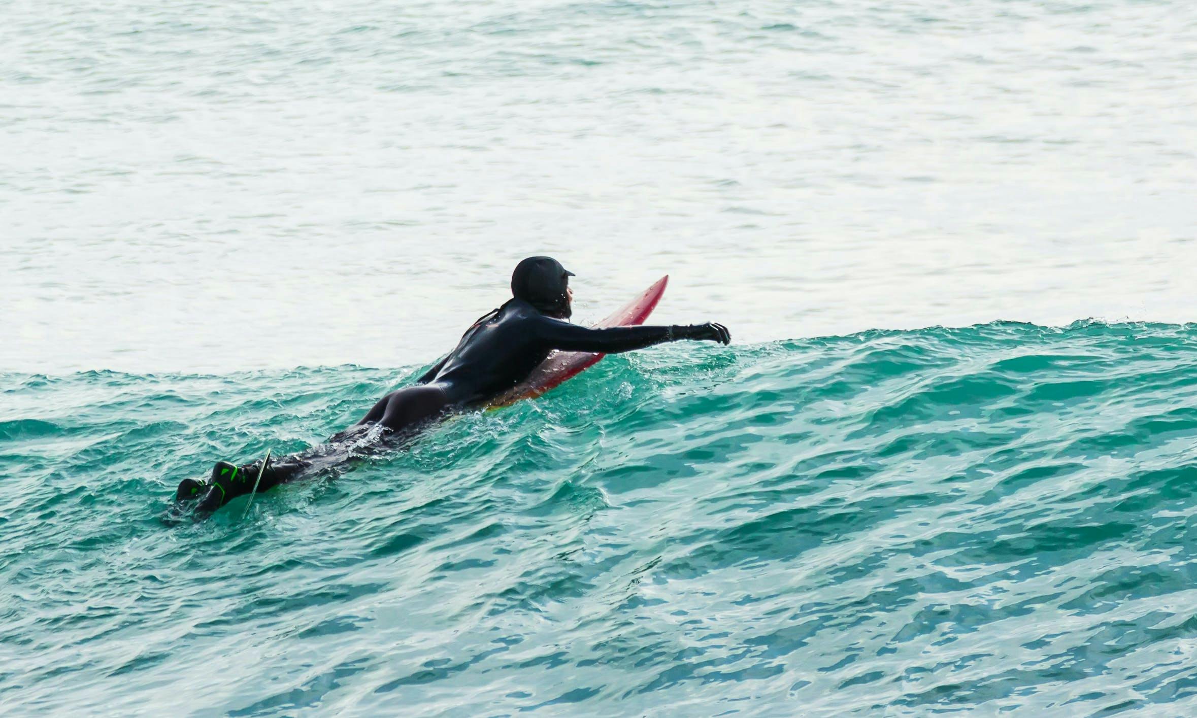 Surfer wearing hood, gloves, booties and wetsuit on a wave