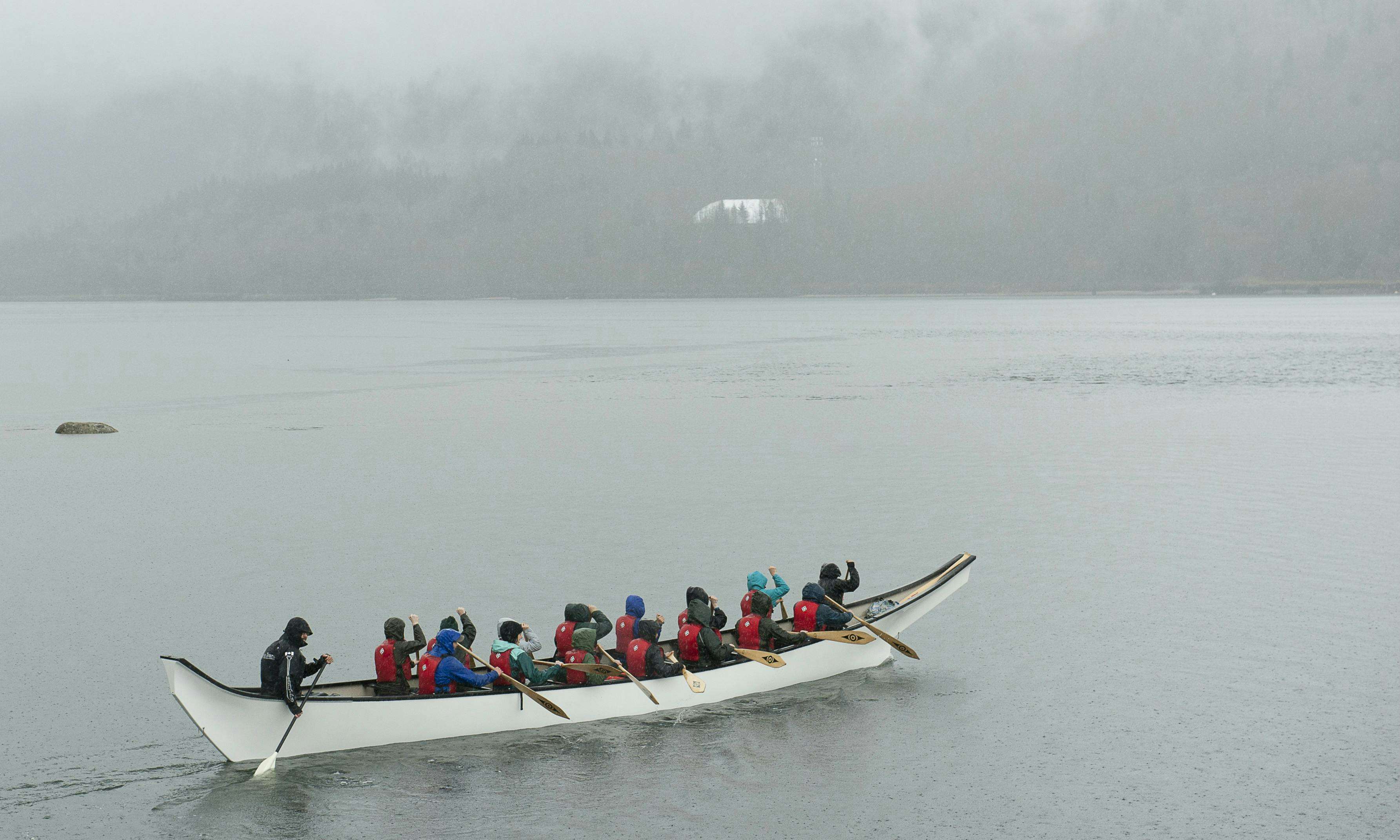 A group of girls paddles a large canoe across an ocean inlet.