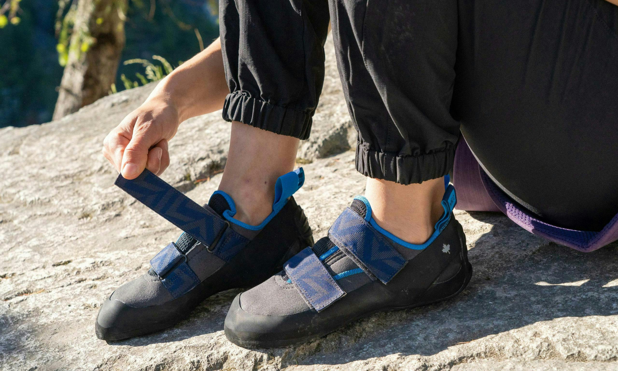 Close up of a person putting on climbing shoes outdoors; the closure on the shoes is Velcro