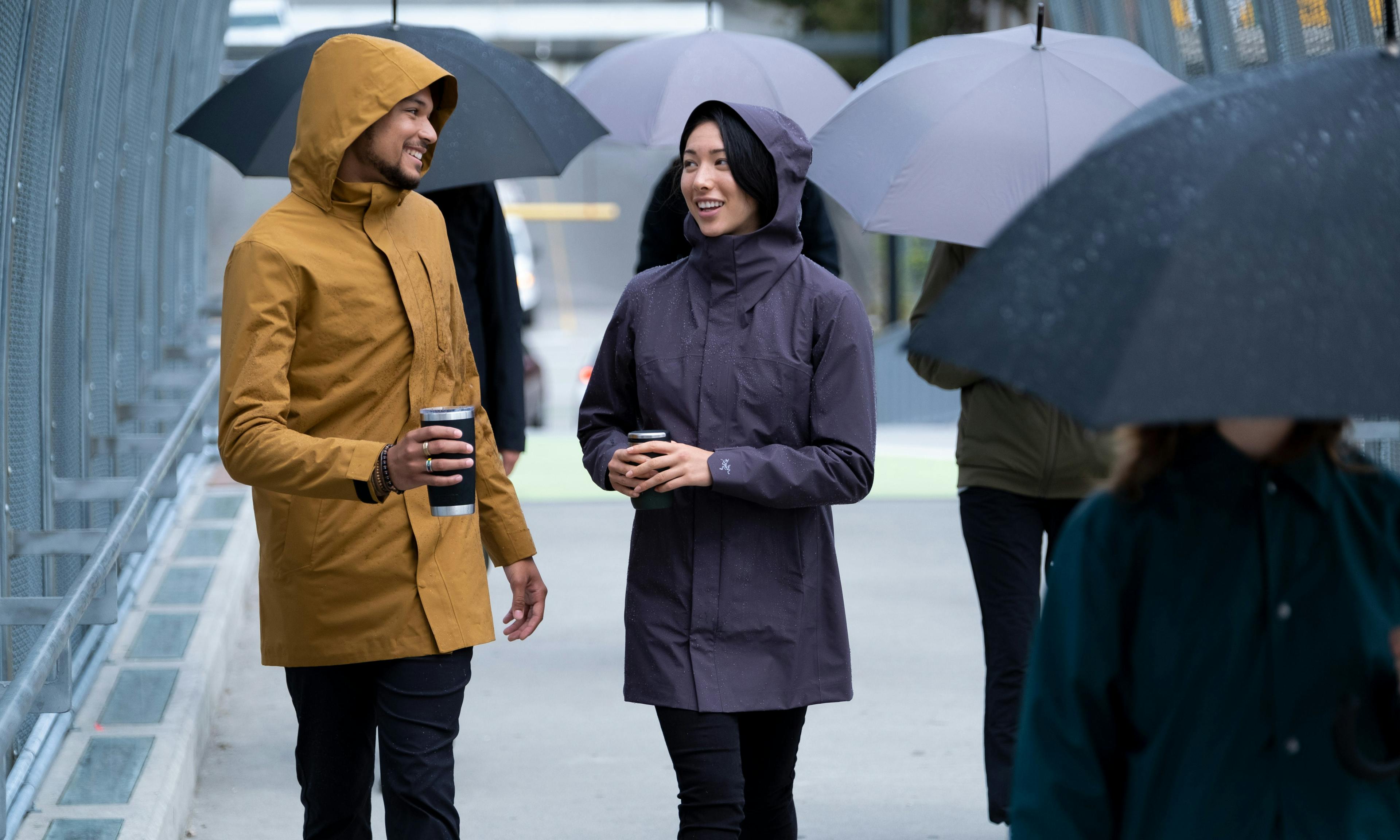 Two people walking on a rainy day wearing jackets to stay dry, while everyone around them is using umbrellas