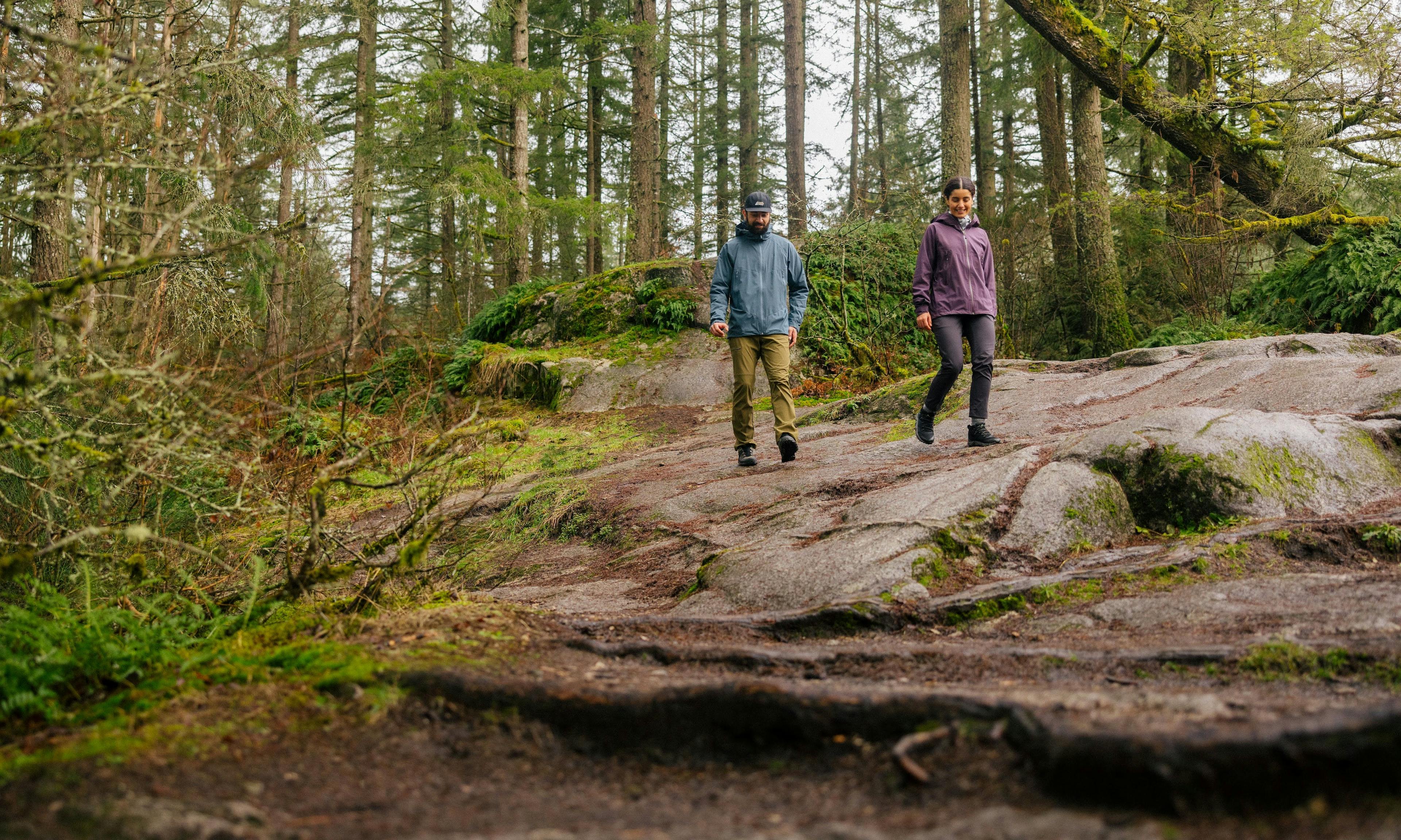 Two hikers in MEC Hydrofoil Jackets on a wet weather walk in the forest