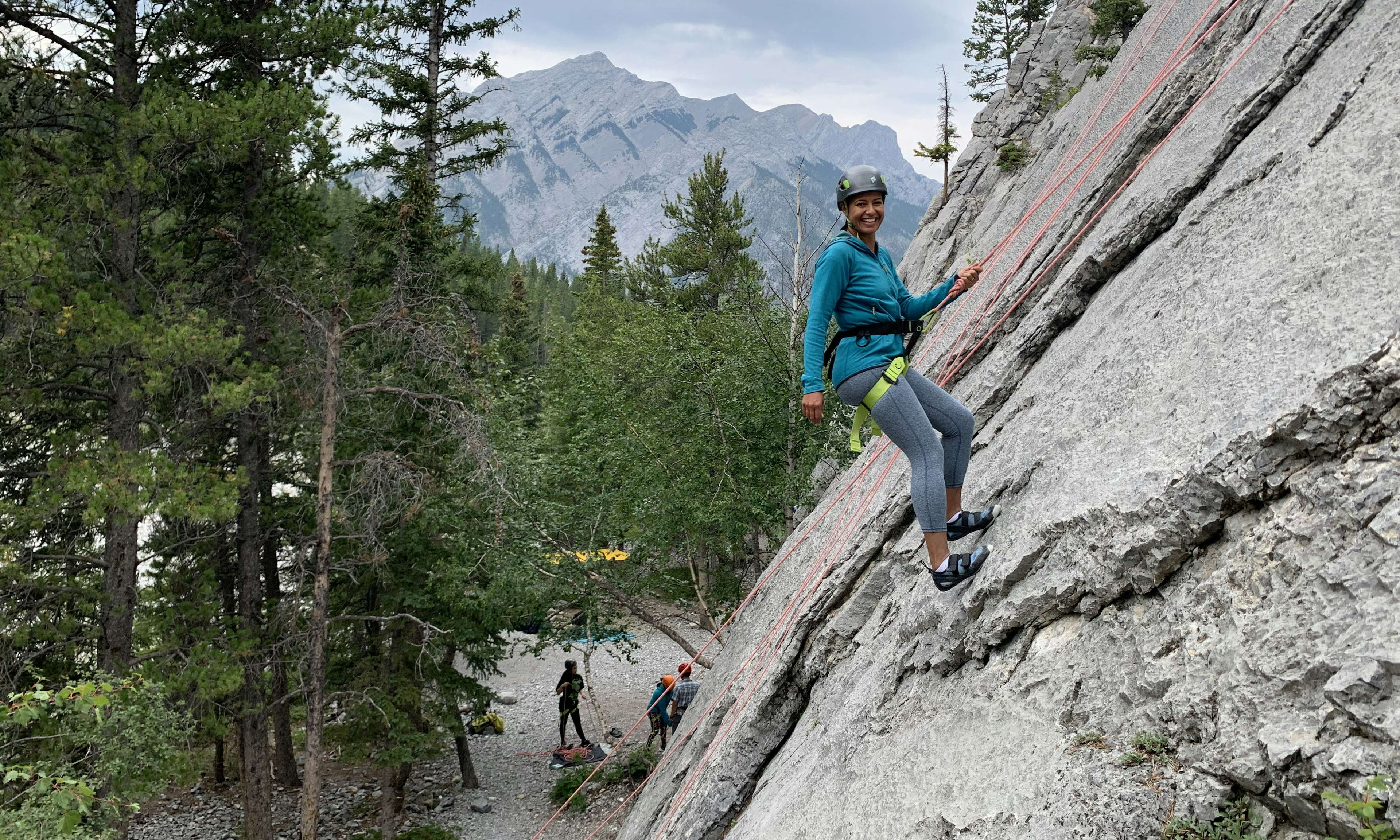 Climber on a rock wall smiling, with mountains in the background