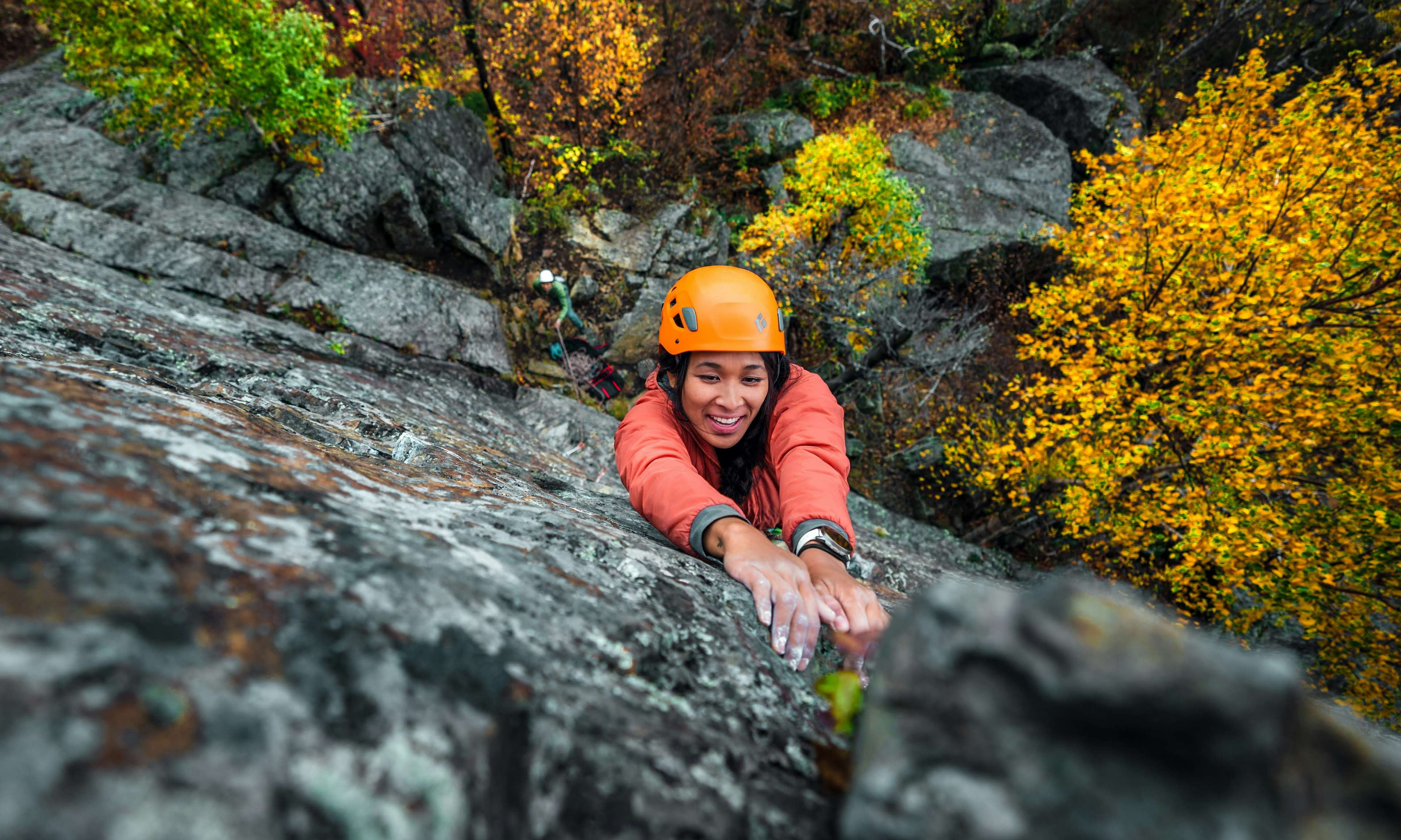 MEC Ambassador Emma Contaoe rock climbing outdoors and grabbing onto a hold with hands covered in chalk