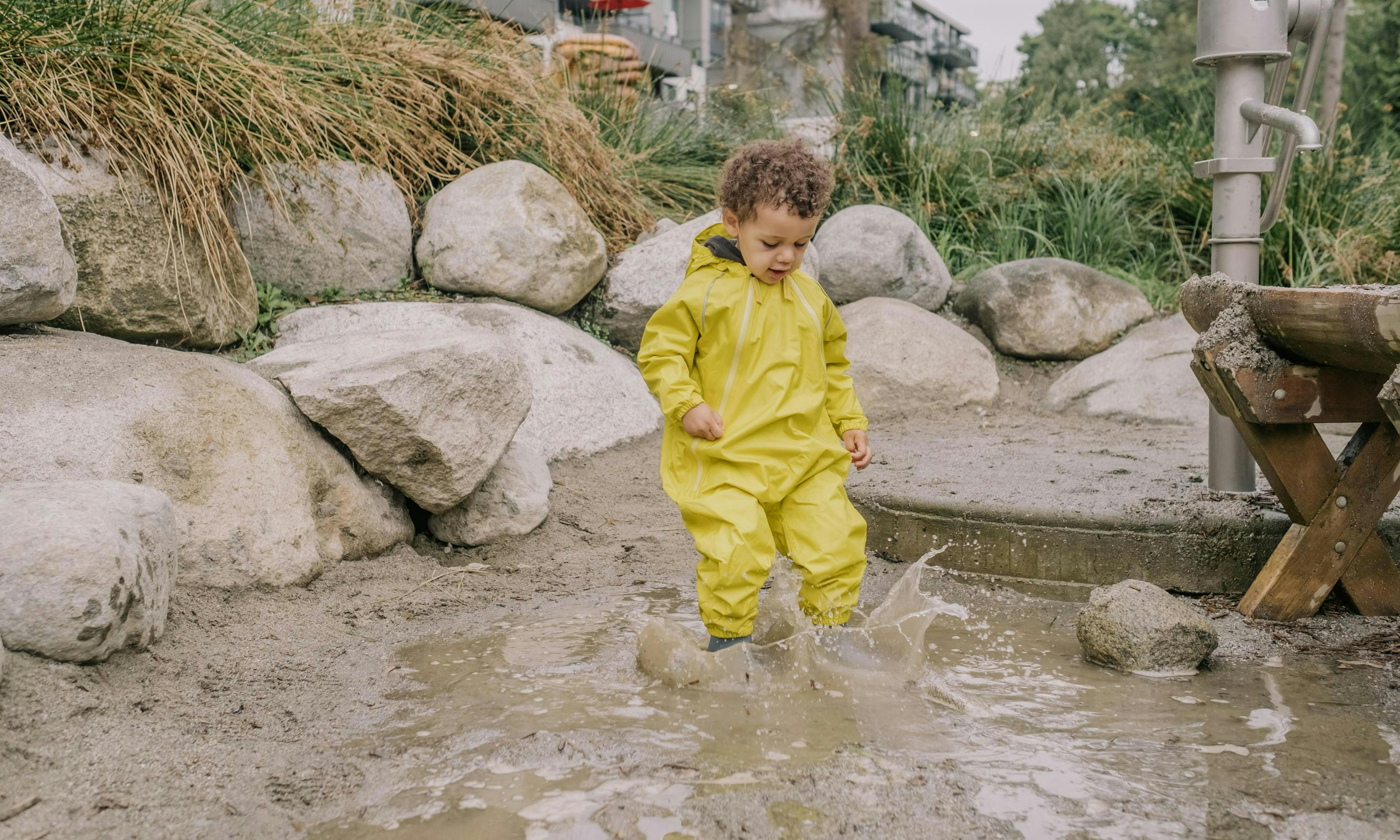 Child splashing in a huge mud puddle and wearing a yellow MEC Newt Suit