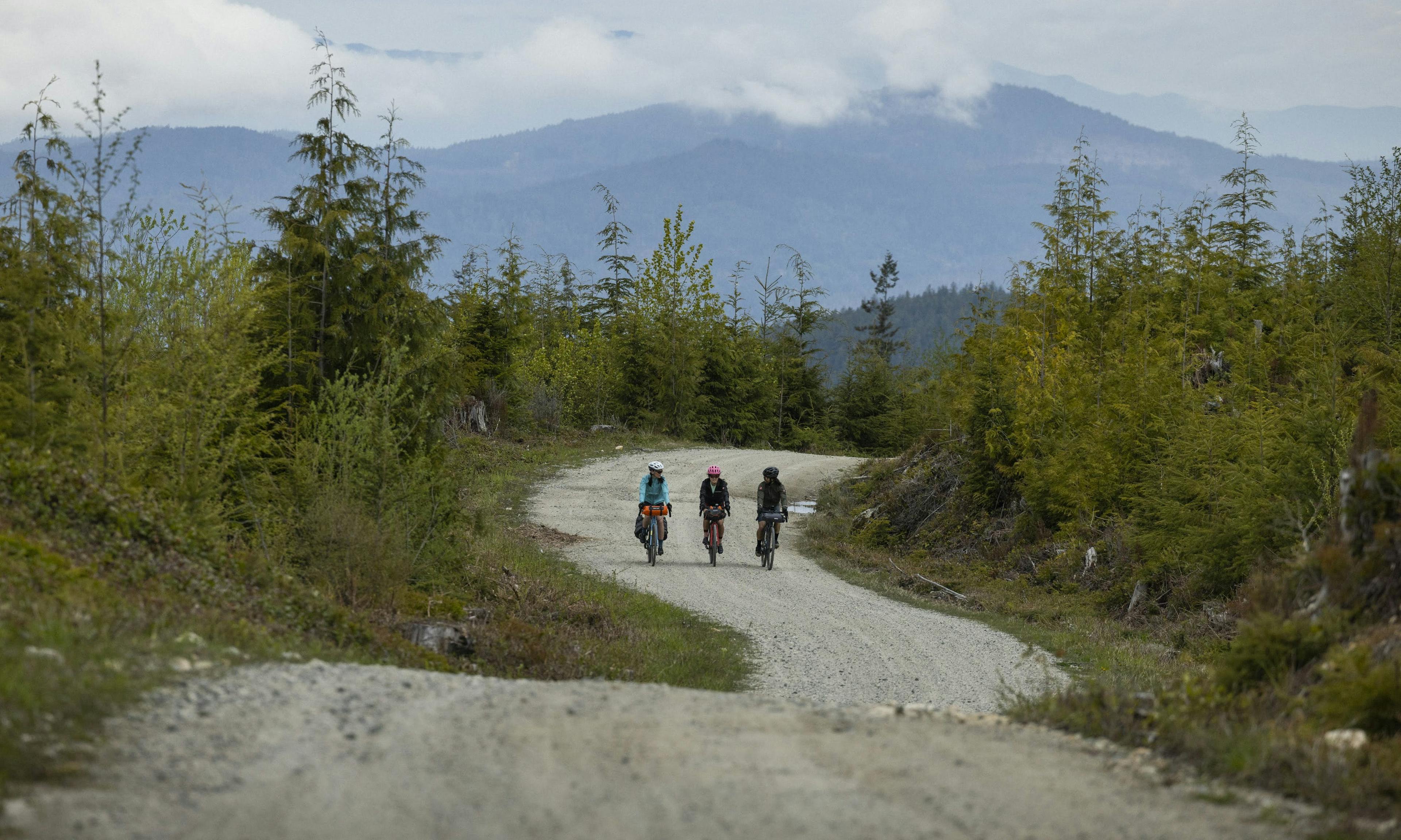 Three cyclists riding on a gravel road with mountain scenery in the background