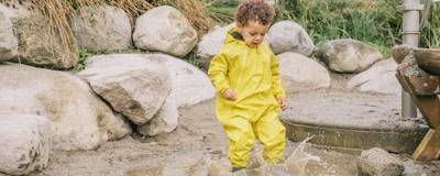 Small child splashing in a puddle wearing a bright yellow rain suit from MEC